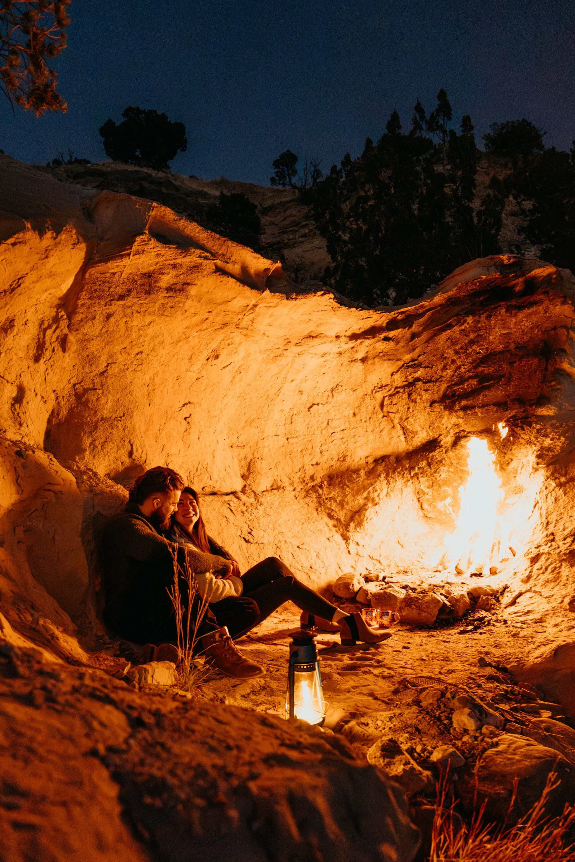 Two people sitting by a campfire in a rocky outdoor setting at night.