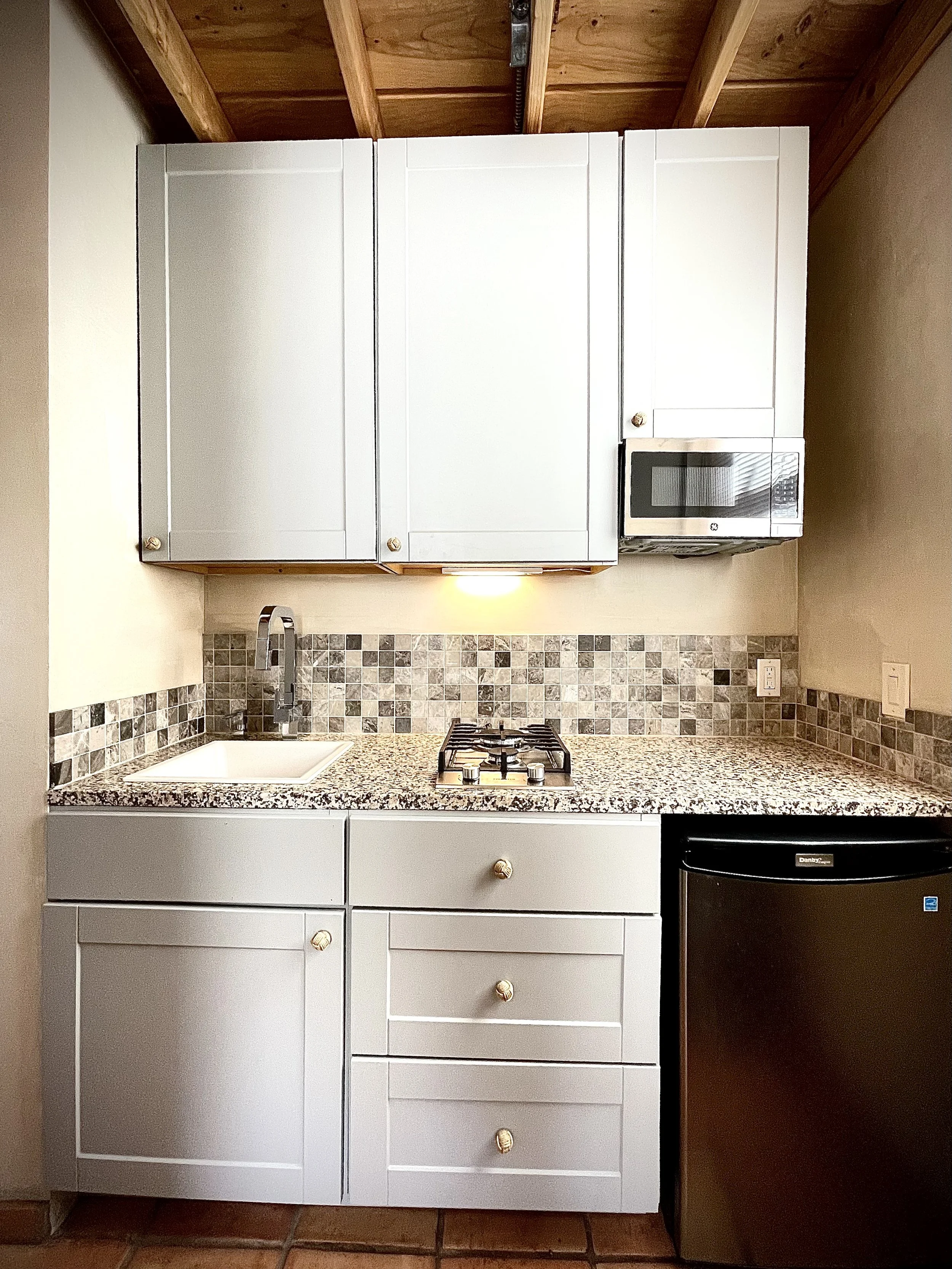 Small kitchen with white cabinets, granite countertop, tiled backsplash, a sink, stove, microwave, and mini refrigerator.