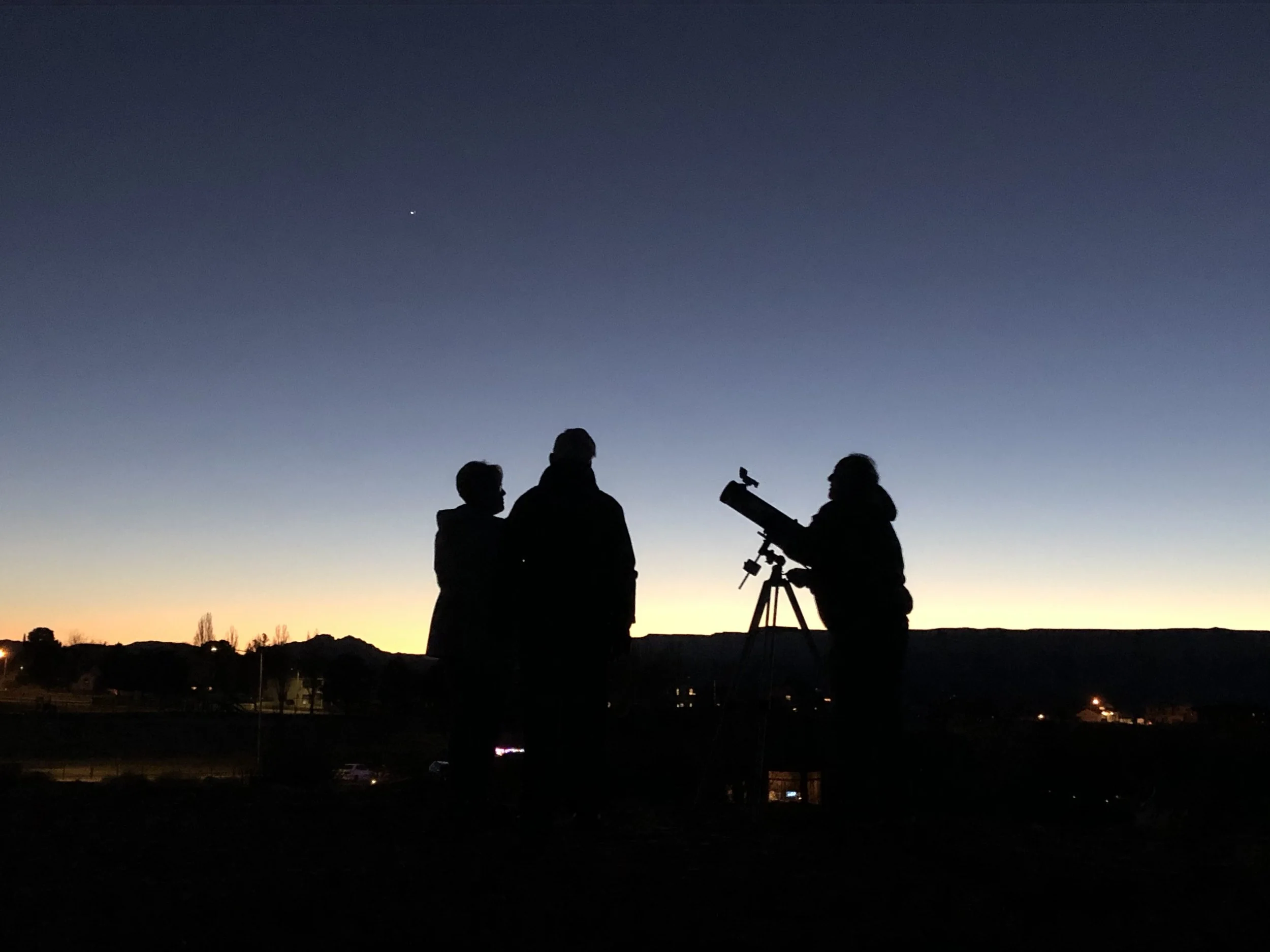 Three silhouetted people against an evening sky with a telescope at Grandview Knoll Trail