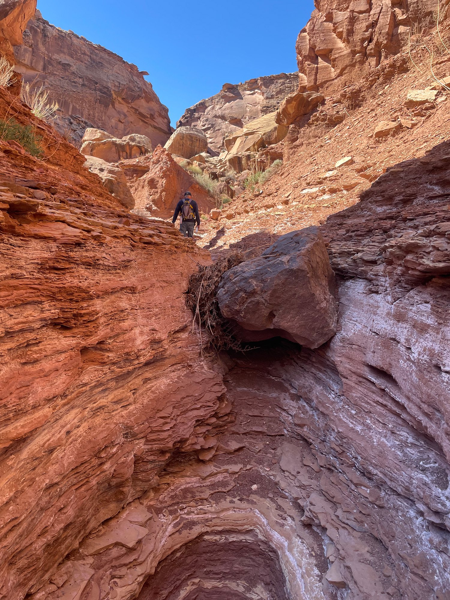 A chock-stone wedged between sanstone wash walls with a hiker in the distance in Upper Cathedral Wash