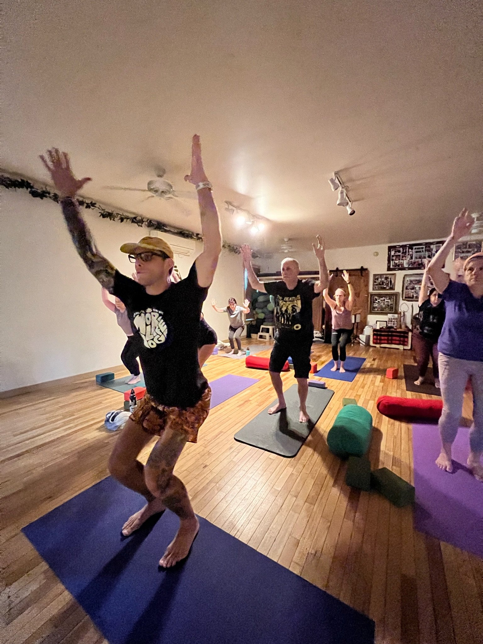 Two people performing yoga poses on a paddleboard in a river surrounded by dense green forest.