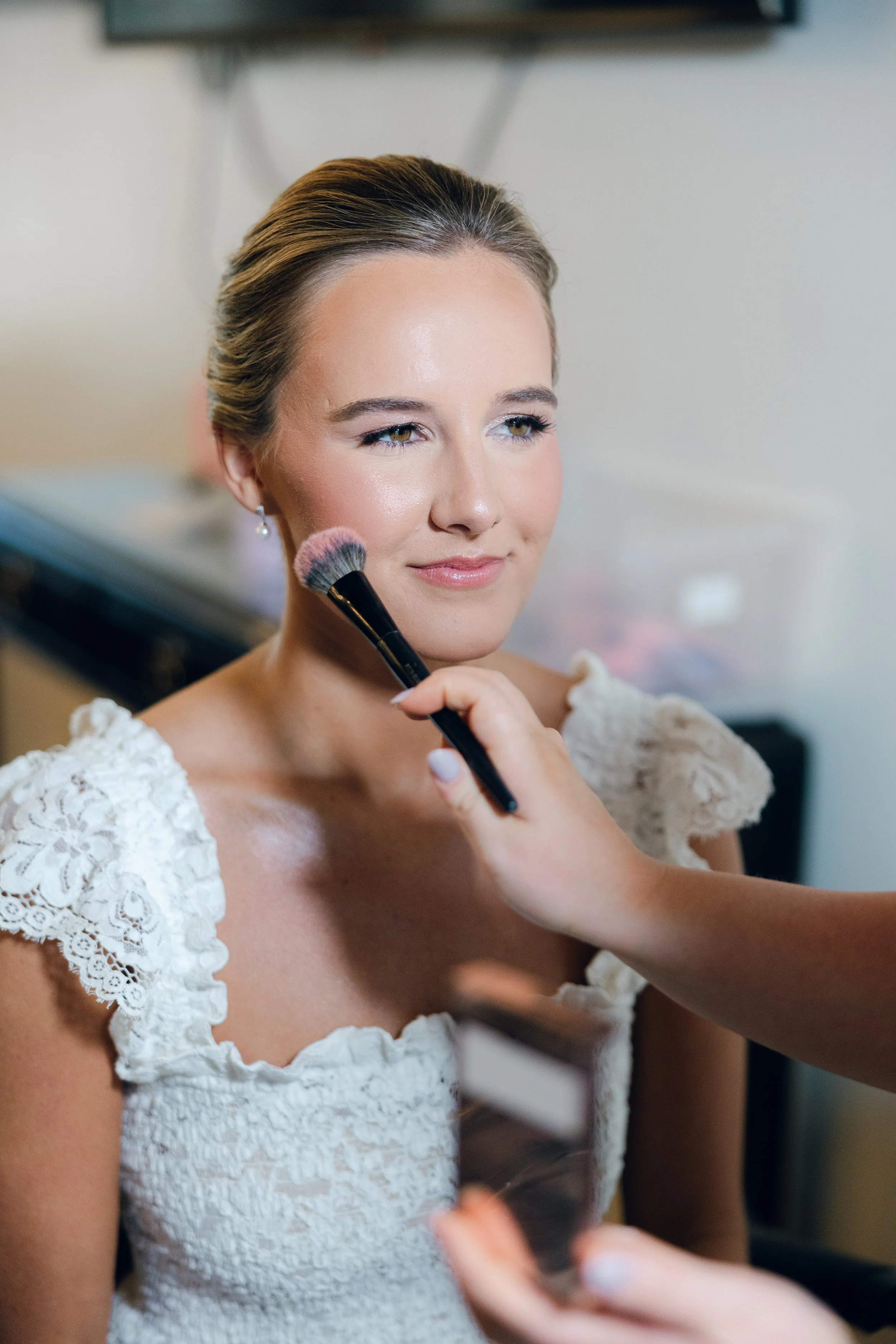 A woman getting her makeup done by a makeup artist in a well-lit room.