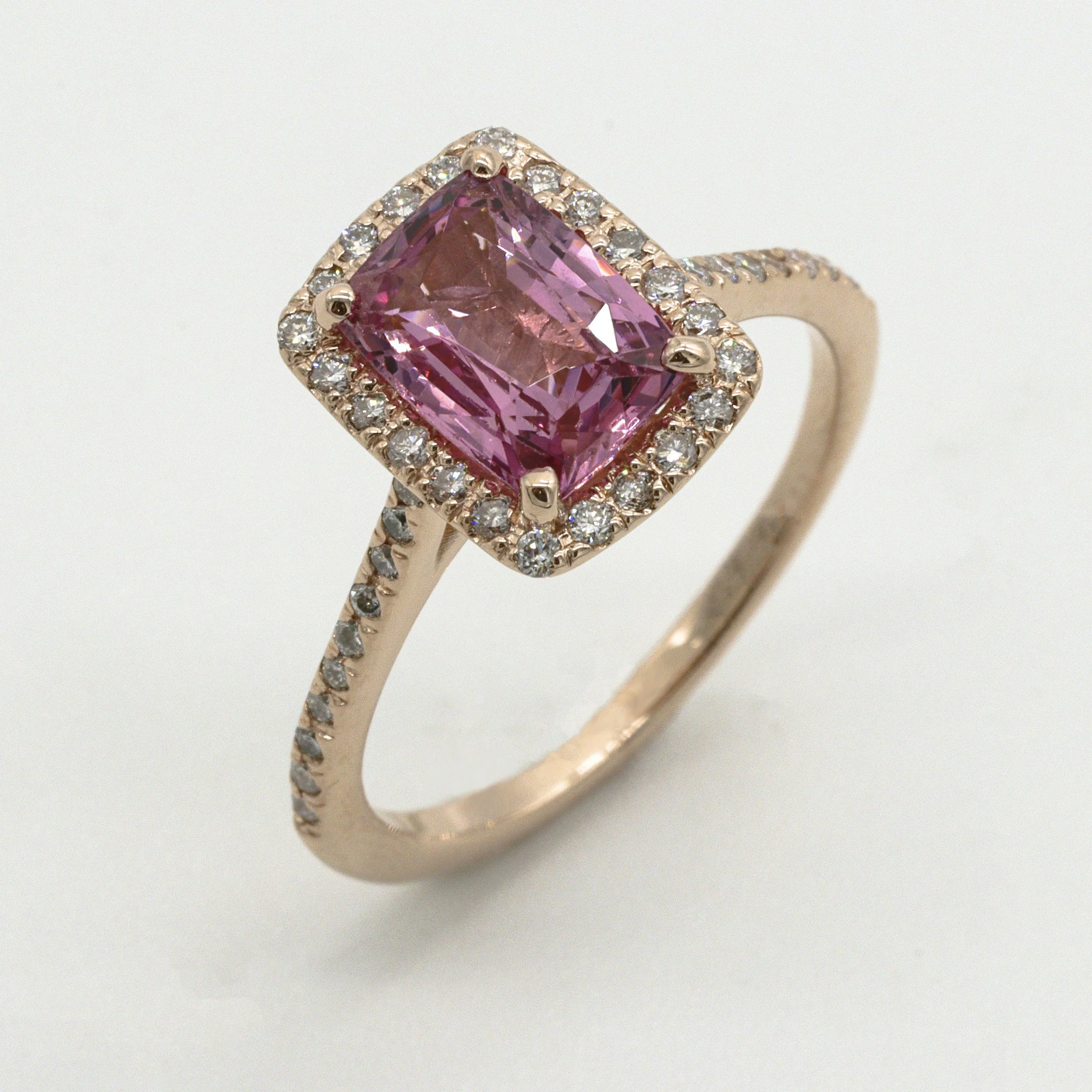 Close-up of a rose gold ring with a large pink rectangular gemstone surrounded by small diamonds.