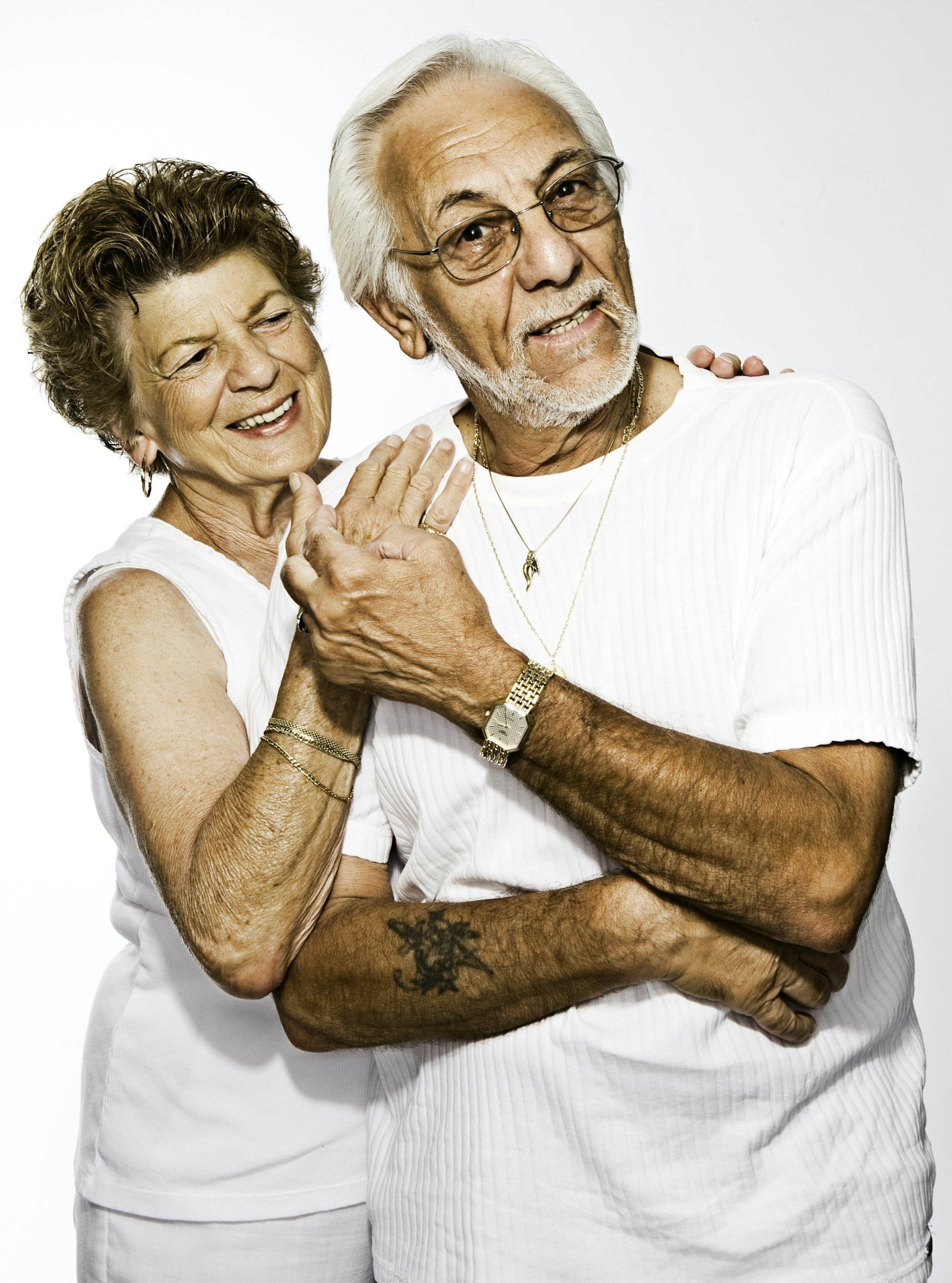 An elderly man and woman smiling and embracing against a plain white background.