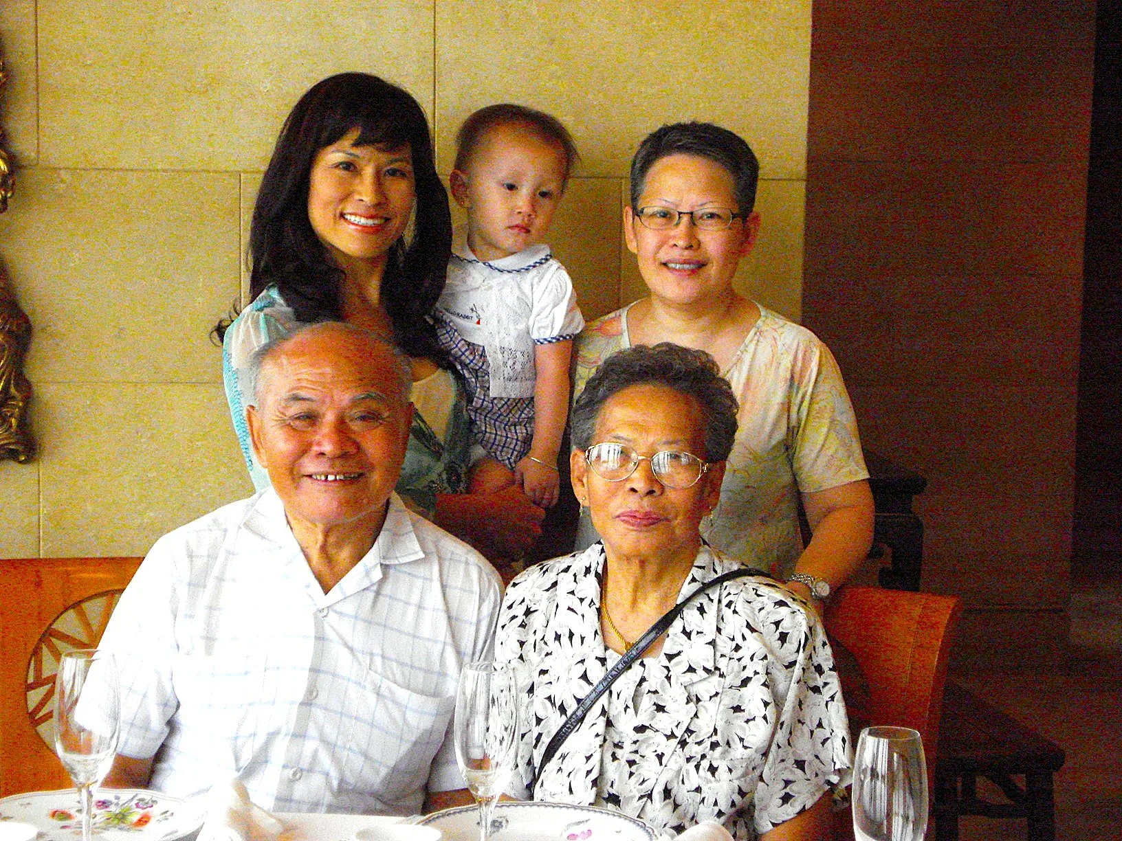 Family group photo with three elderly adults, a young woman, and a small child in a restaurant setting.