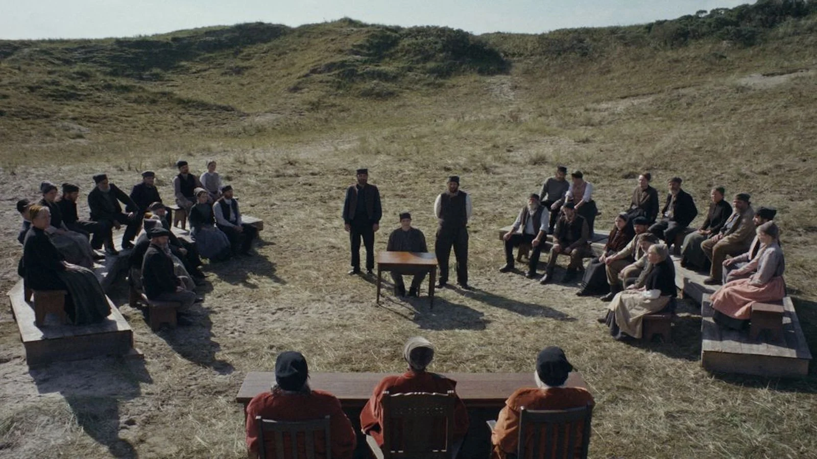 Still from Trial of Hein with a group of people in a field, seated in a courtroom arrangement