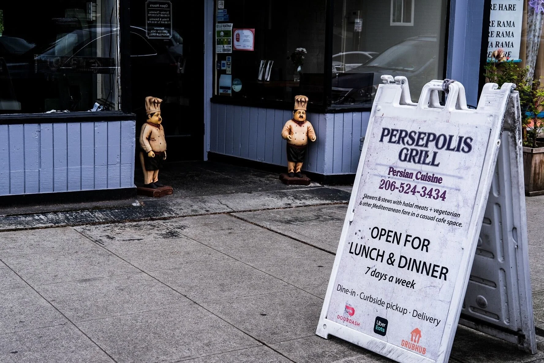 entrance to Persepolis Grill in U District; a white sandwich board on the sidewalk, two chef statues on either side of the front door