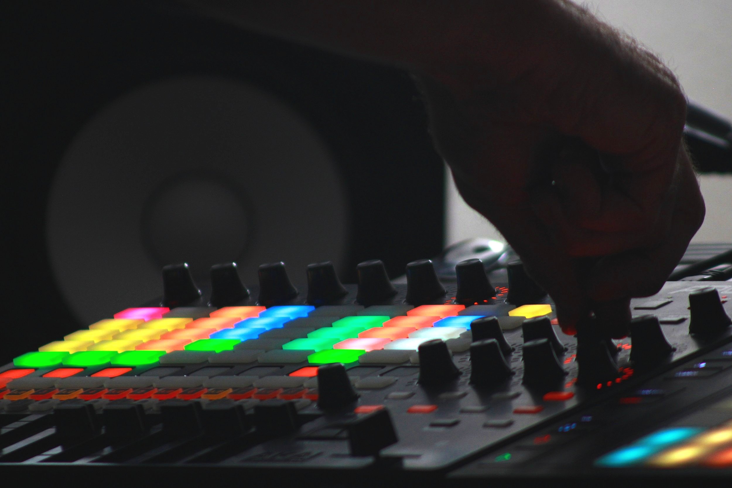 Close-up of a DJ's hand adjusting controls on a colorful electronic music production mixer with illuminated buttons.