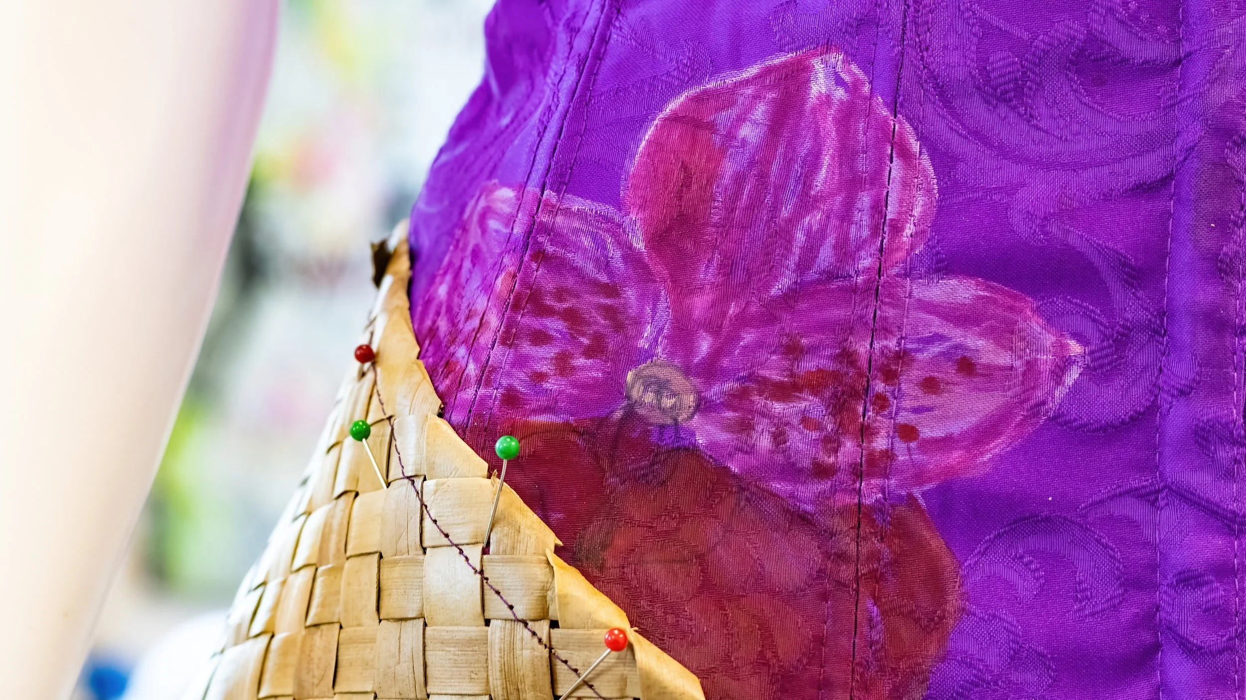 Close-up of a woven basket with a purple fabric lining decorated with patterns, and multicolored pins securing the fabric to the basket.