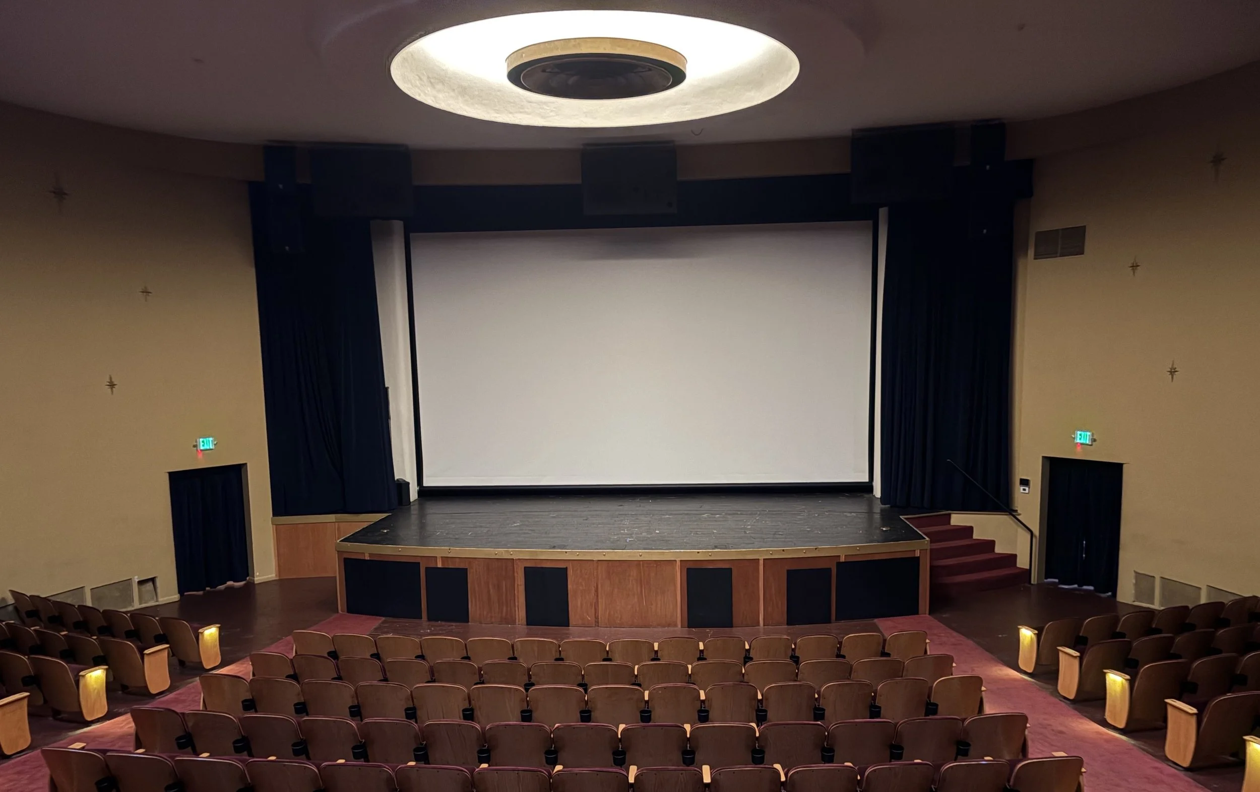 auditorium with black curtain-lined movie screen, sloped seating, stage in front of screen