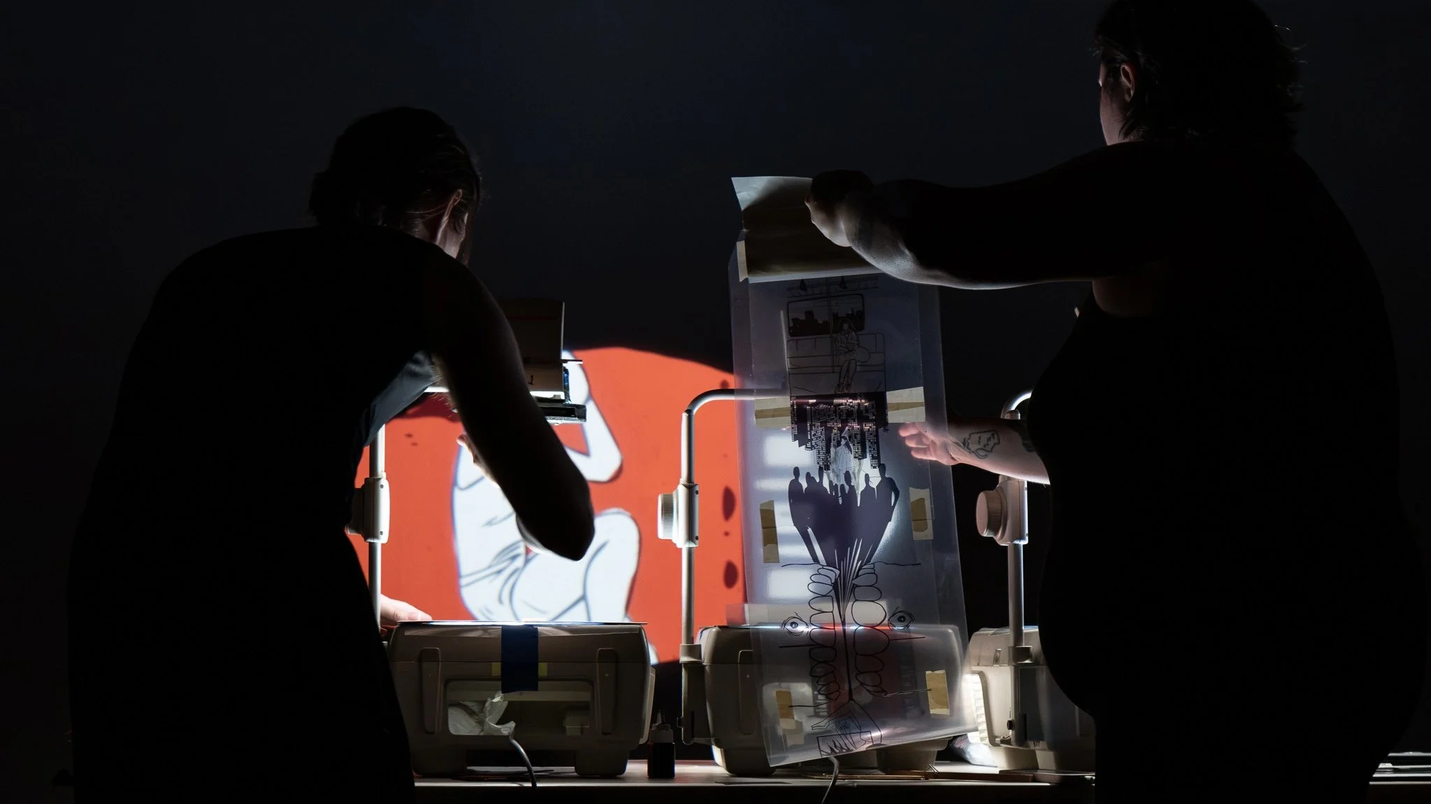 two people use overhead projectors and images on transparencies to show artwork on a screen