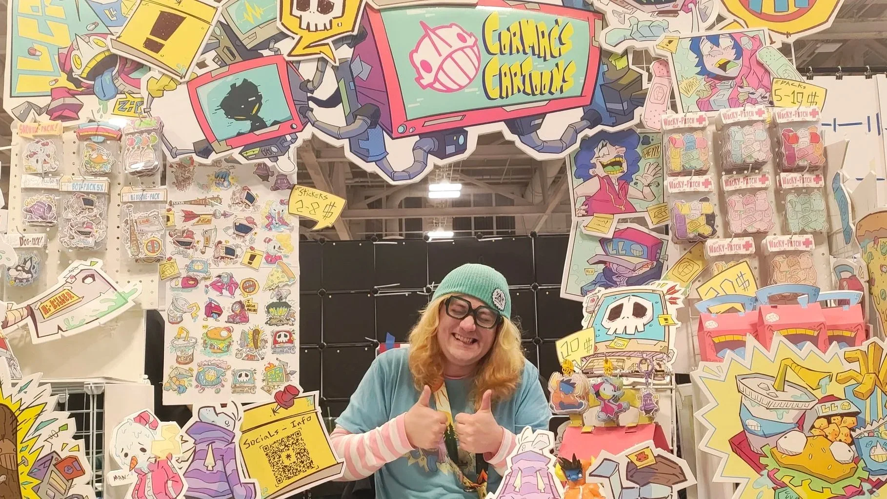 Cormac Cartoons booth with Cormac holding thumbs up while surrounded by their art