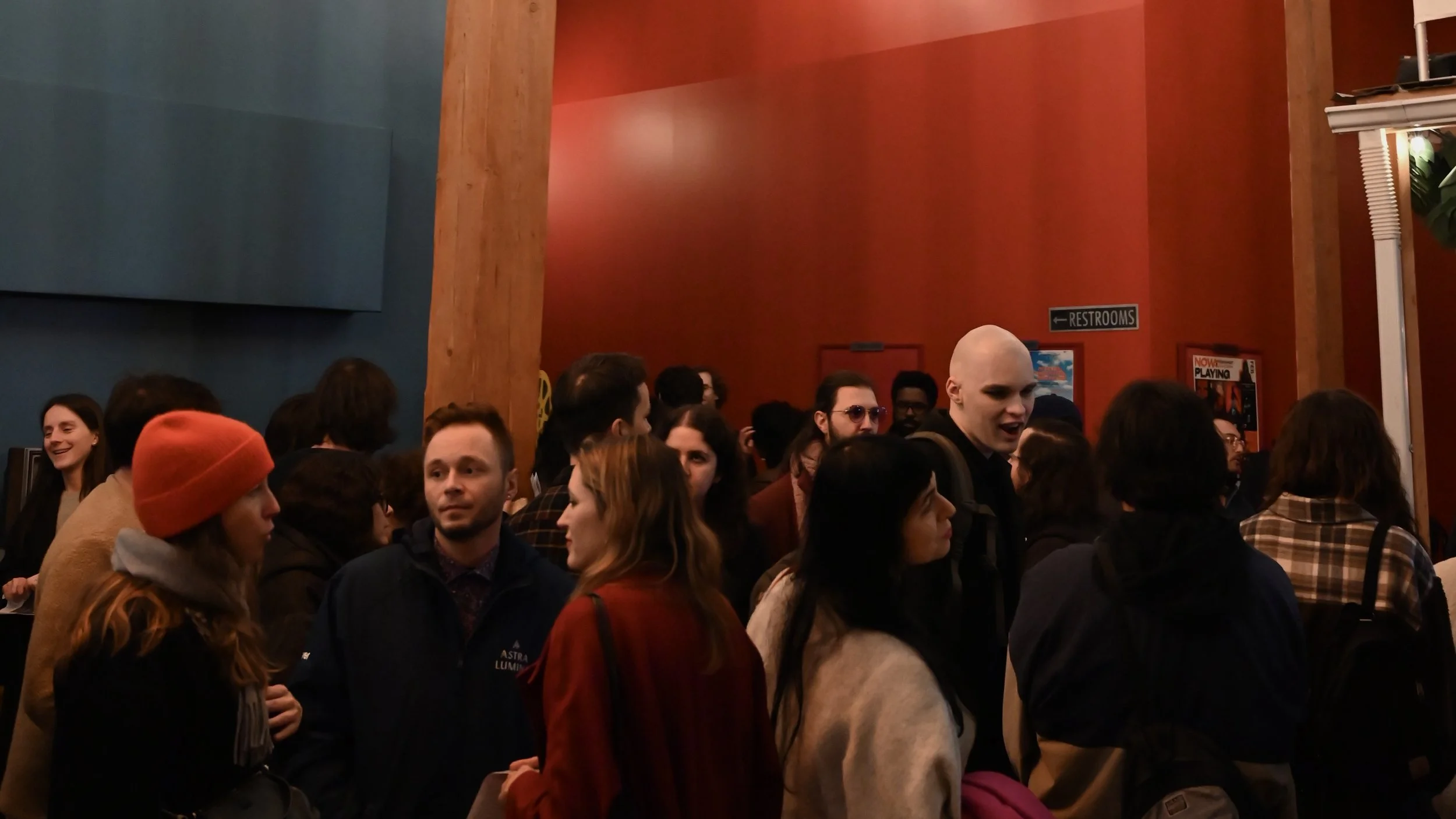 Crowd in lobby of NWFF for Locals Only showcase. Red and blue walls with movie posters.
