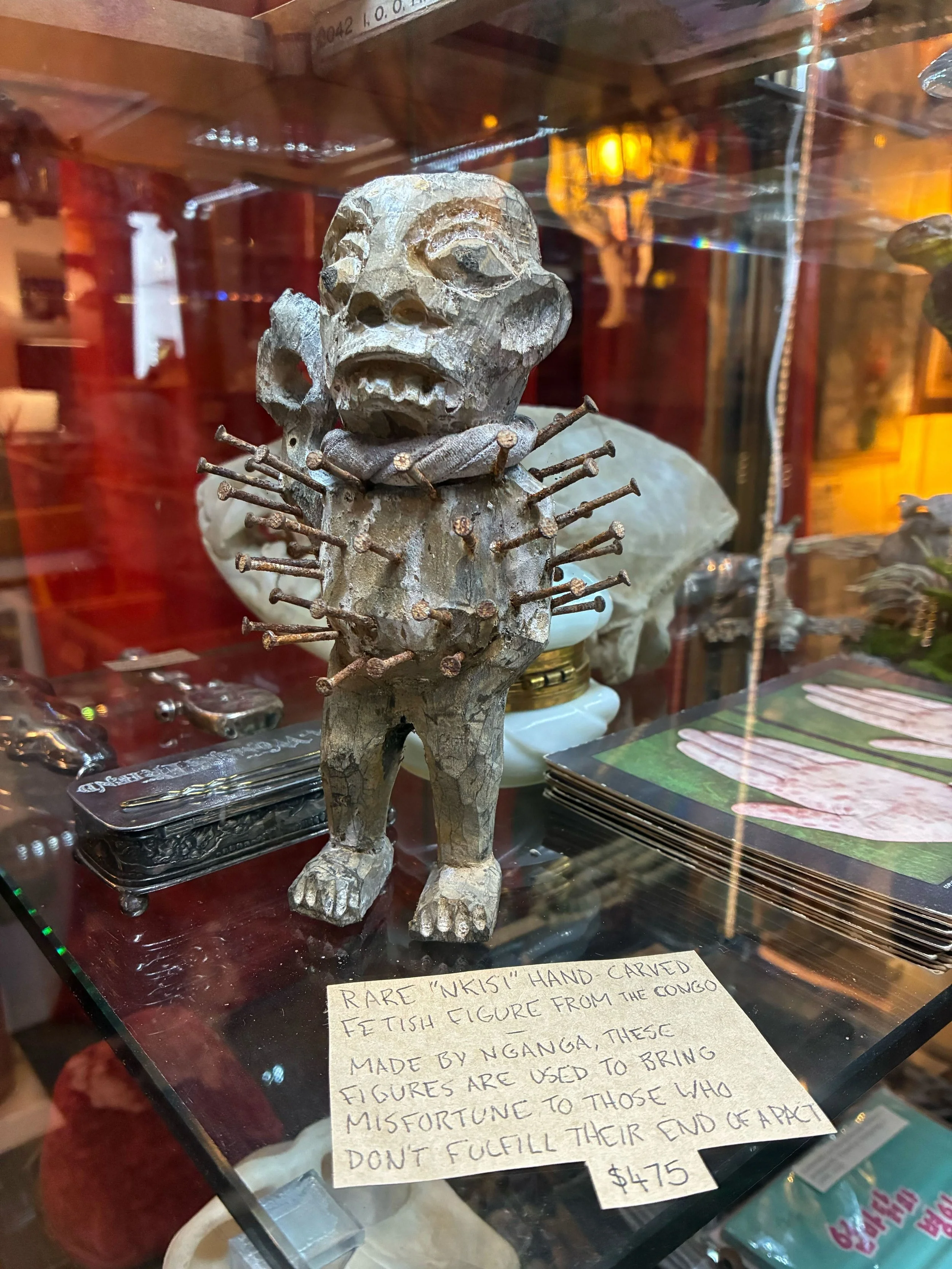 wooden Nkisi doll from Congo, with nails protruding from it and a cloth around its neck