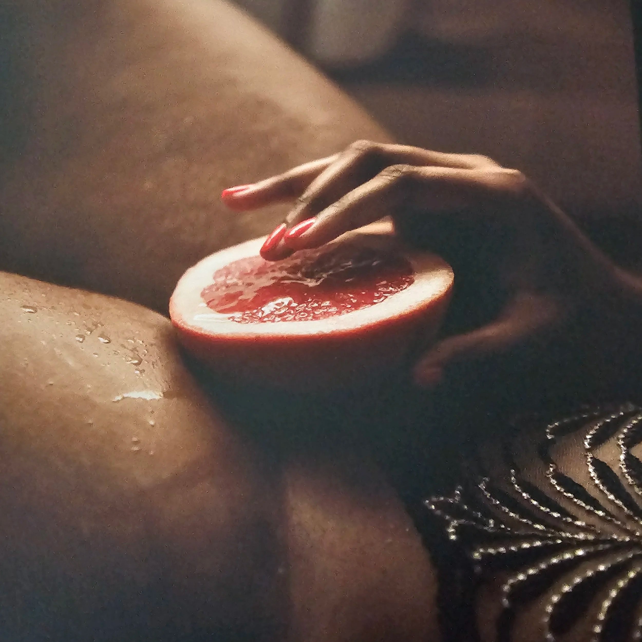 brown legs and a hand with red-painted nailed holding half of a citrus fruit