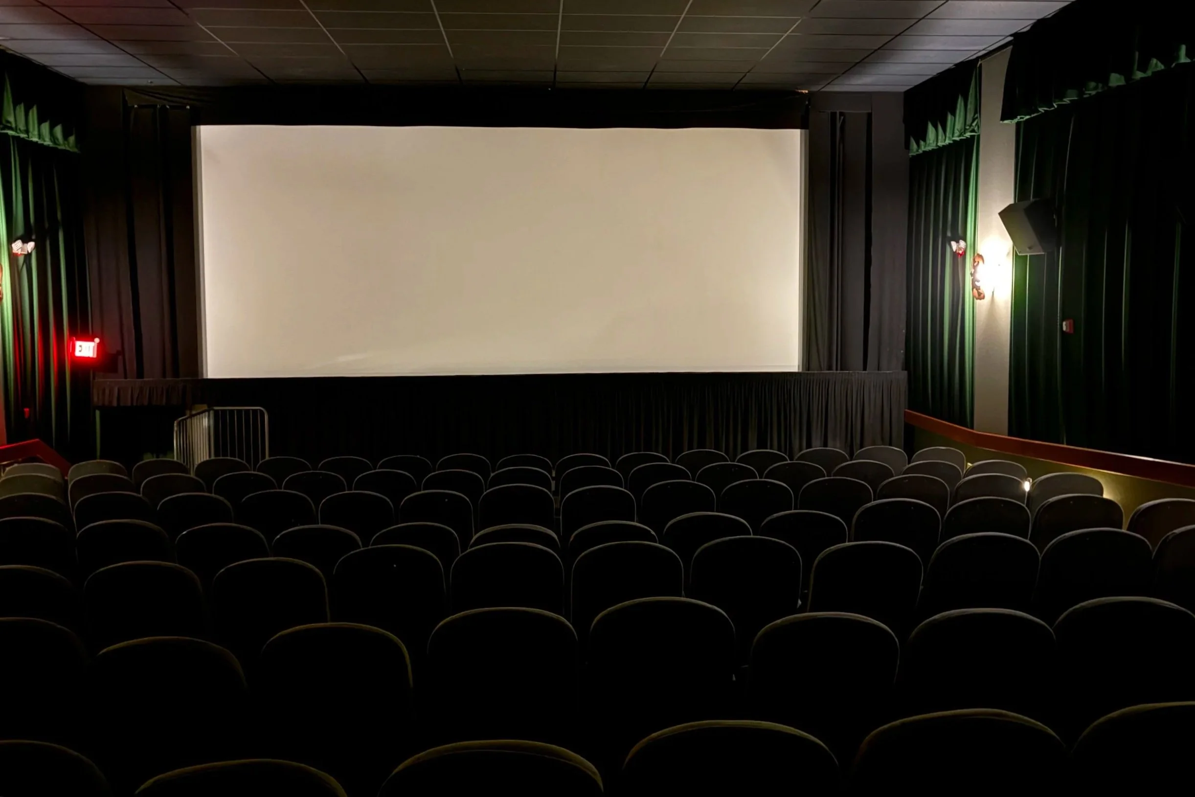auditorium with POV facing movie screen from behind rows of theater seats, dark green curtains on left and right walls