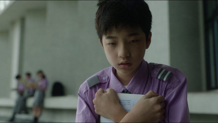 a boy in a purple top holds a book to his chest in Deadline