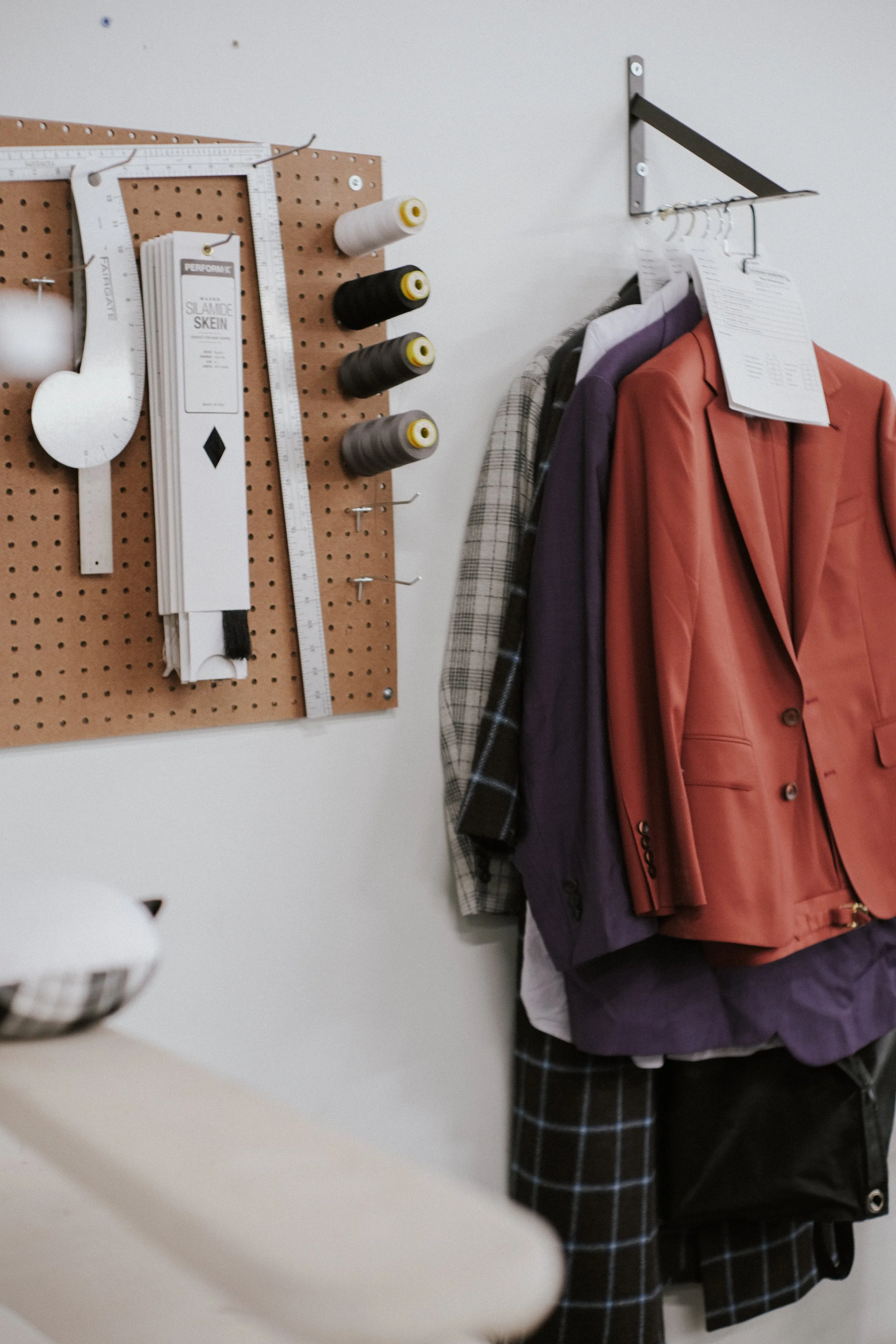 sewing and tailoring supplies hanging on a wall next to suit jackets in progress