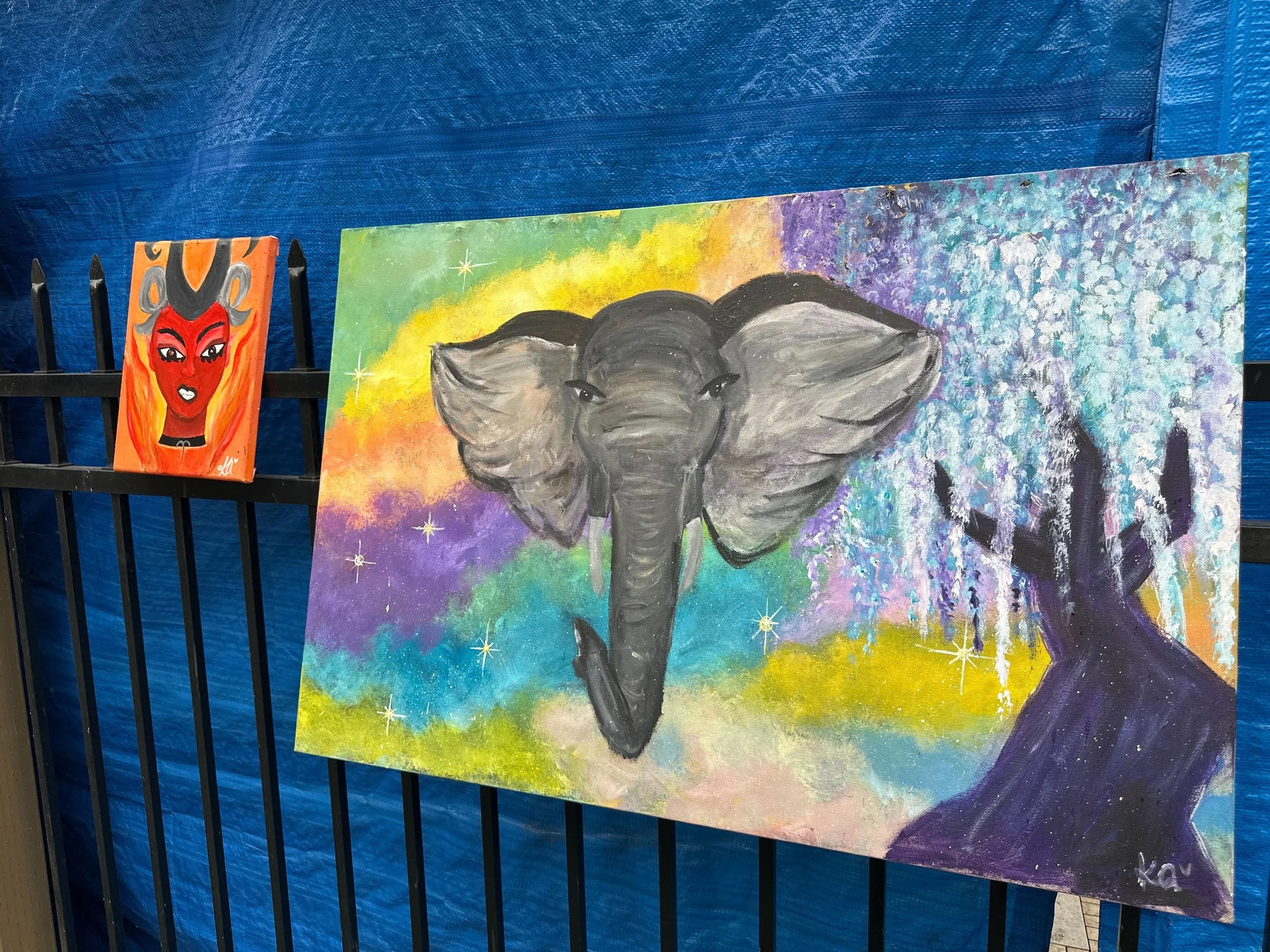 paintings hanging on a fence, one of an elephant and another of femme face