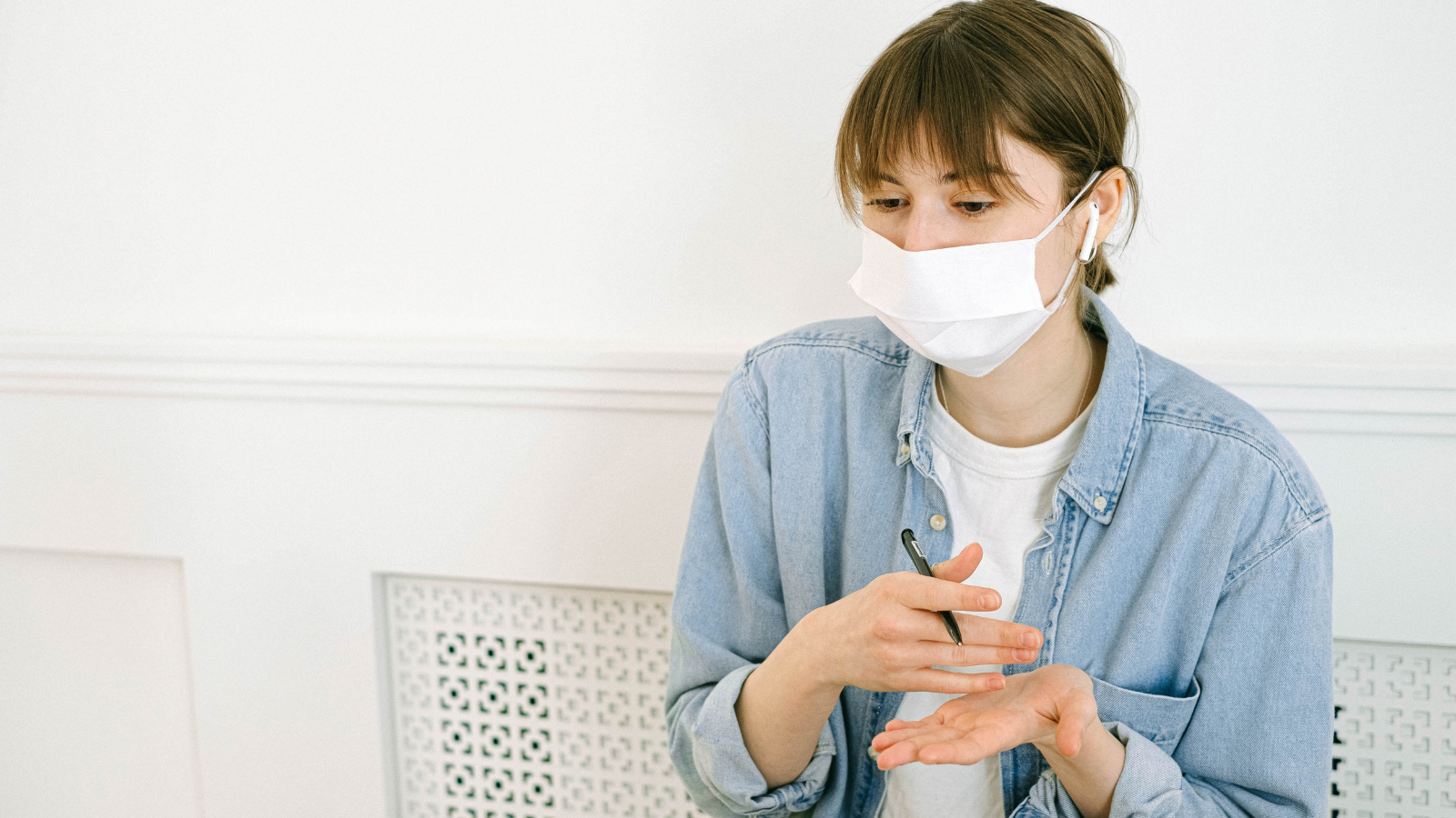 person in a mask holding a pen in a white room