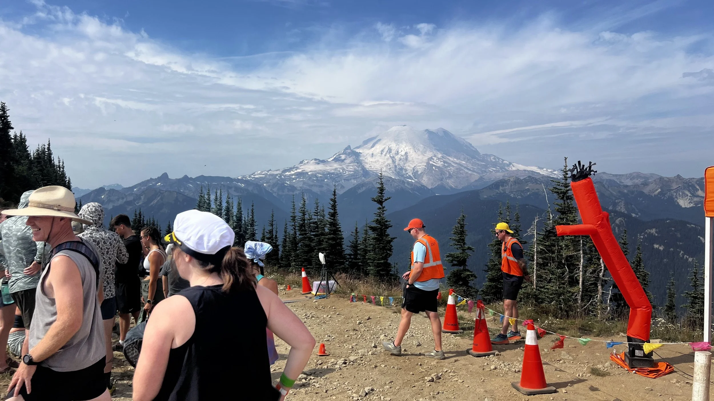 people milling about on a dirt trail, Mt. Tahoma in background under white cloud blanket
