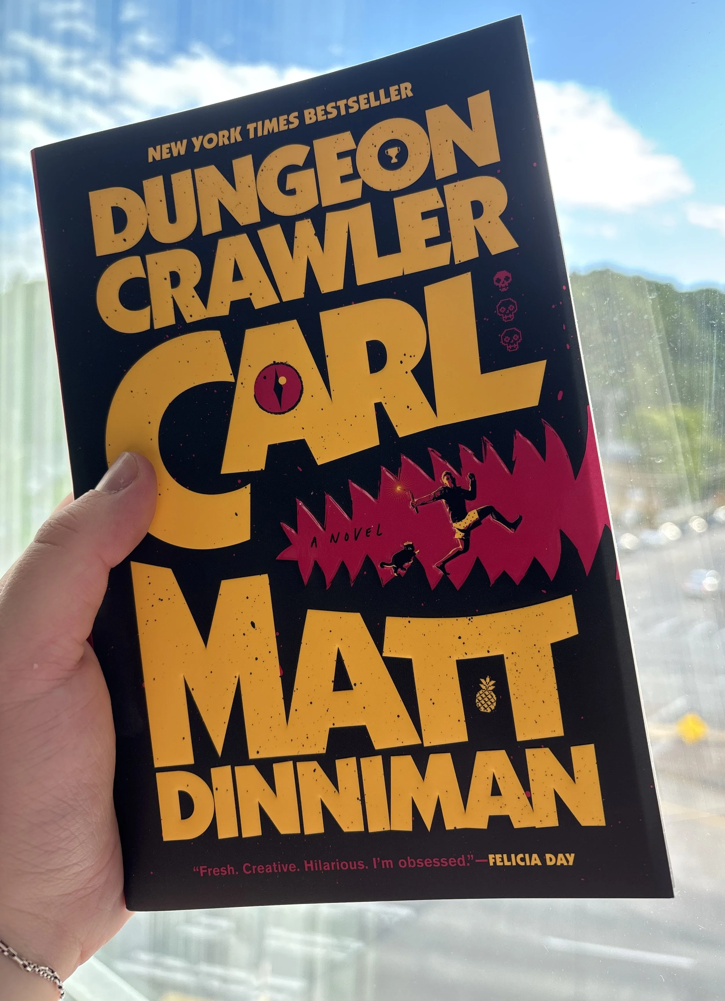 paperback of Dungeon Crawler Carl held up to a window