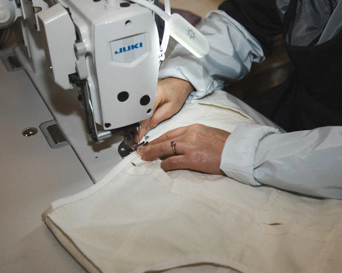 A worker crafting a garment at a sewing machine, hands near the needle and sleeves rolled up at the wrists.