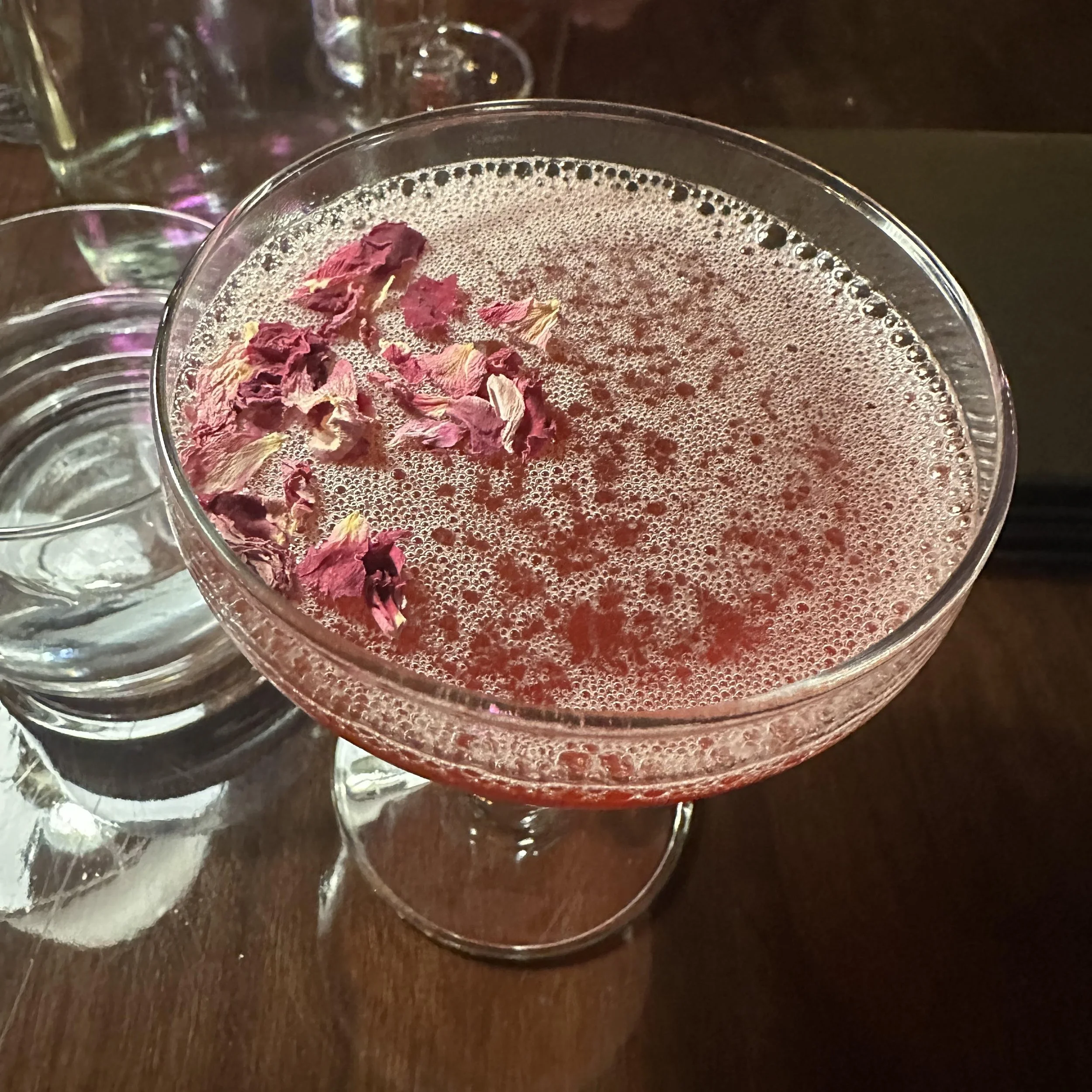 Daisy'y Downfall, a pink beverage with flower petal garnish served in a coupe glass