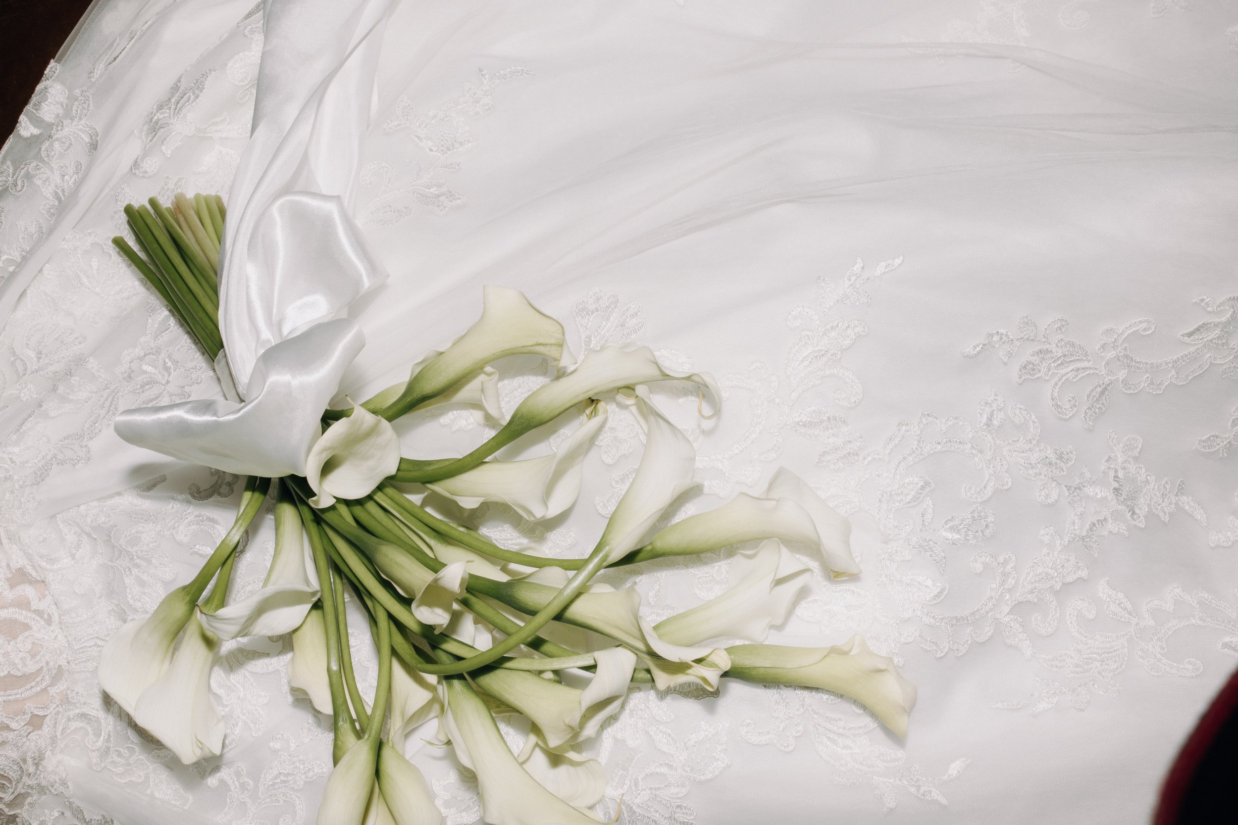 Close-up of a bridal bouquet of white calla lilies on a lace wedding dress.