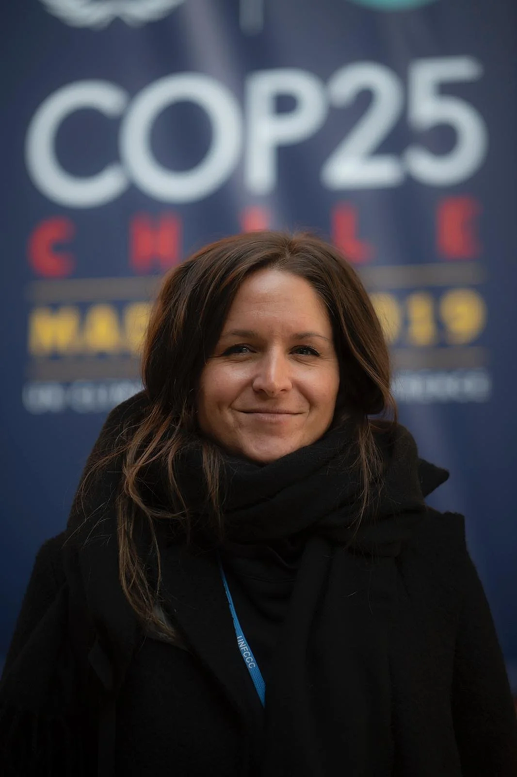 Woman with brown hair smiling, wearing a black coat and scarf at COP25 Climate Change conference
