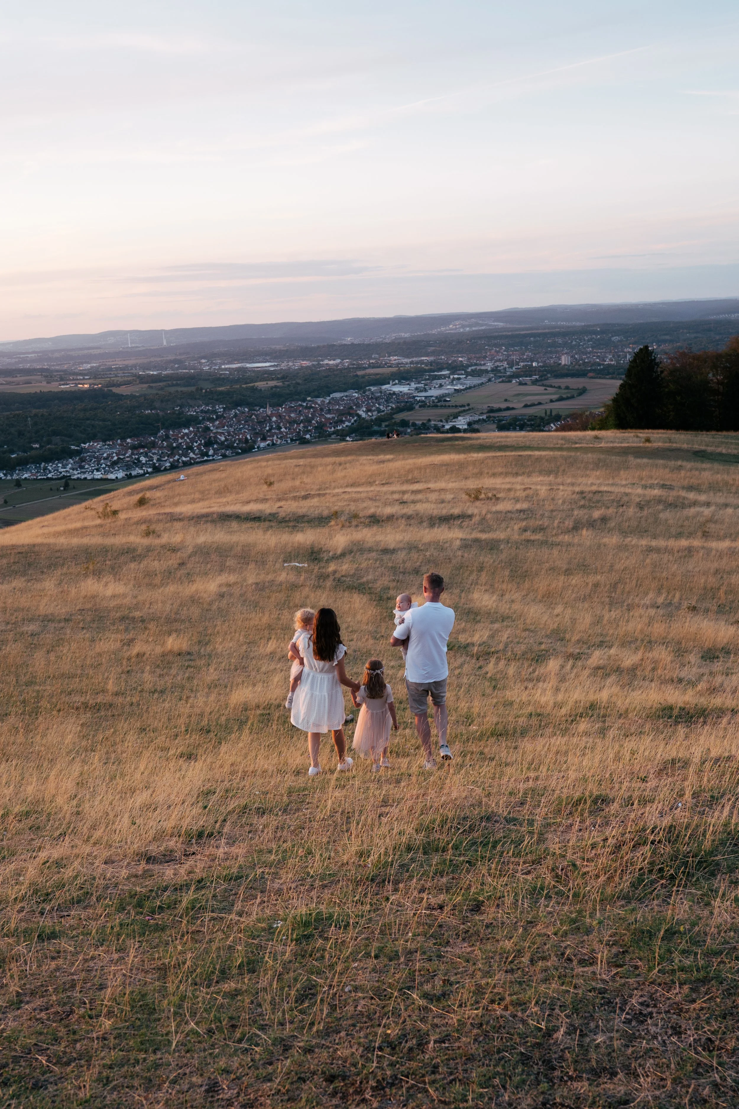 Familie mit Kindern beim Spaziergang auf einem Hügel bei Sonnenuntergang, Blick auf eine Stadt im Tal.