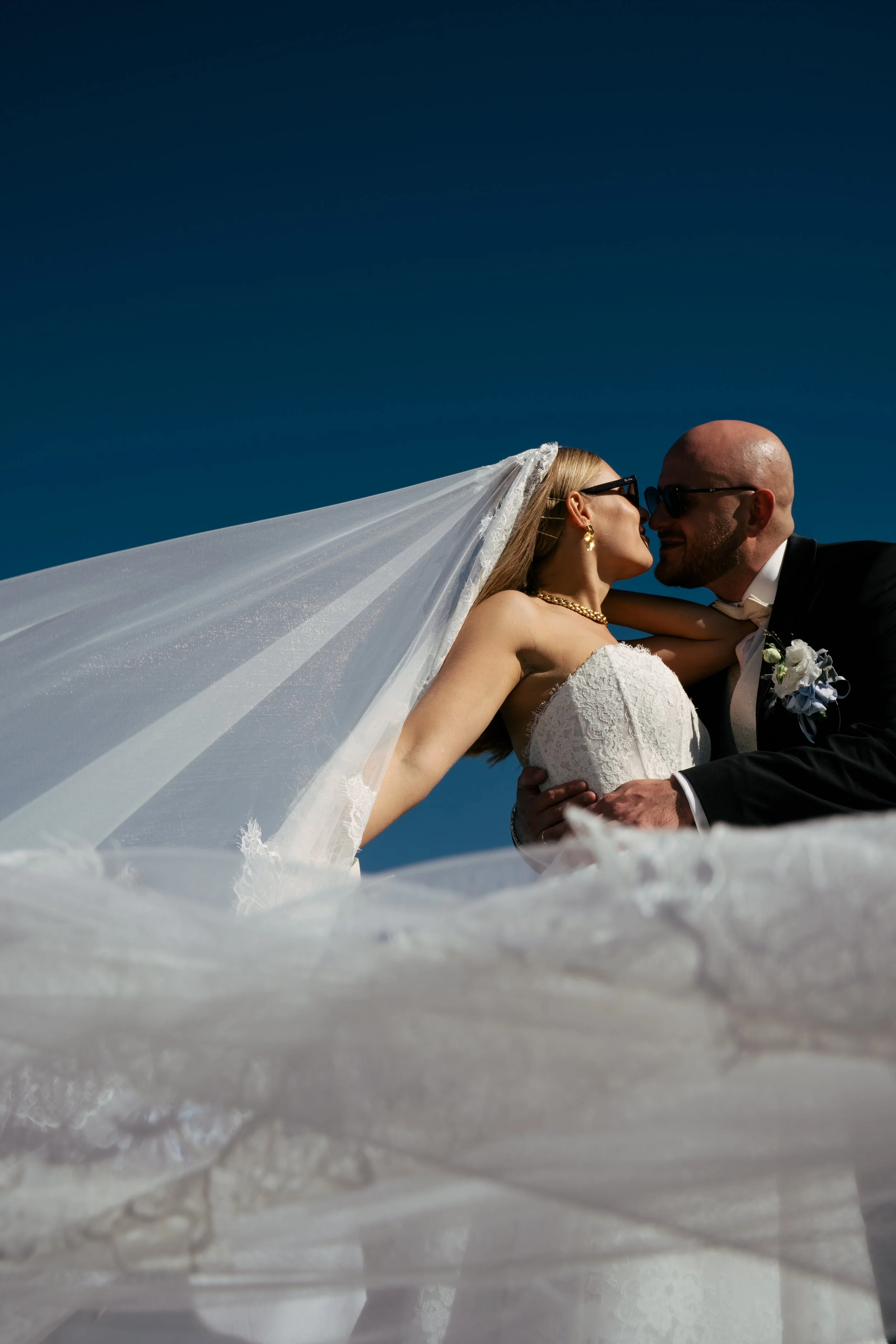 Ein Brautpaar küsst sich bei einer Hochzeit im Freien unter blauem Himmel.