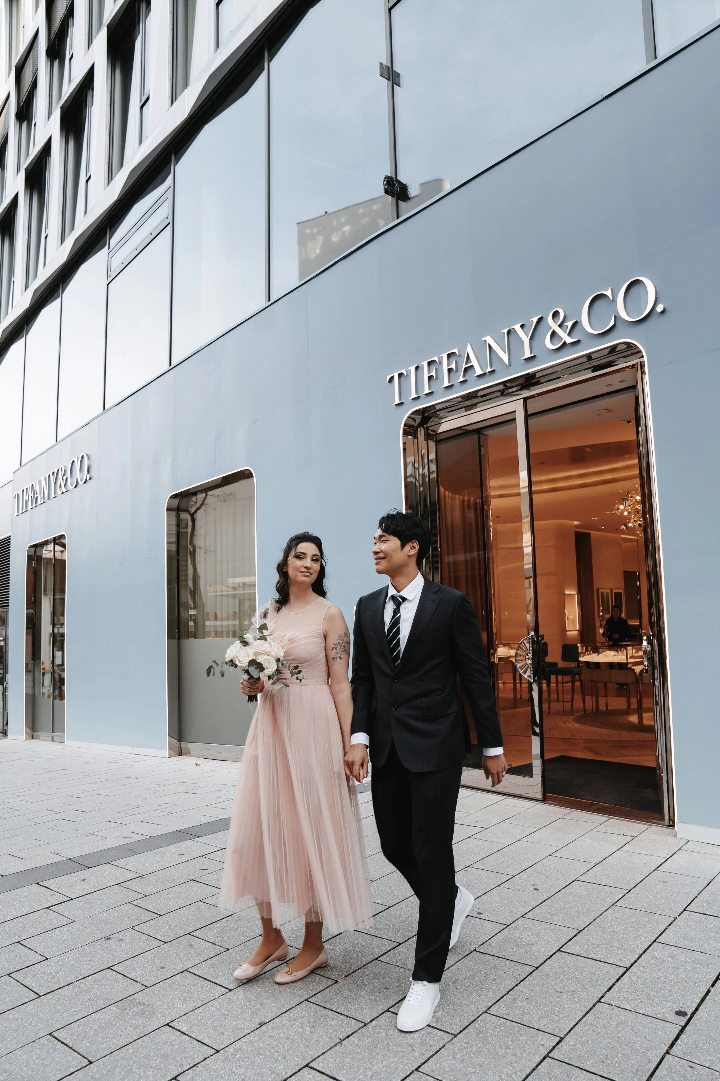 Ein Paar in eleganter Kleidung hält Händchen vor einem Tiffany & Co.-Geschäft.