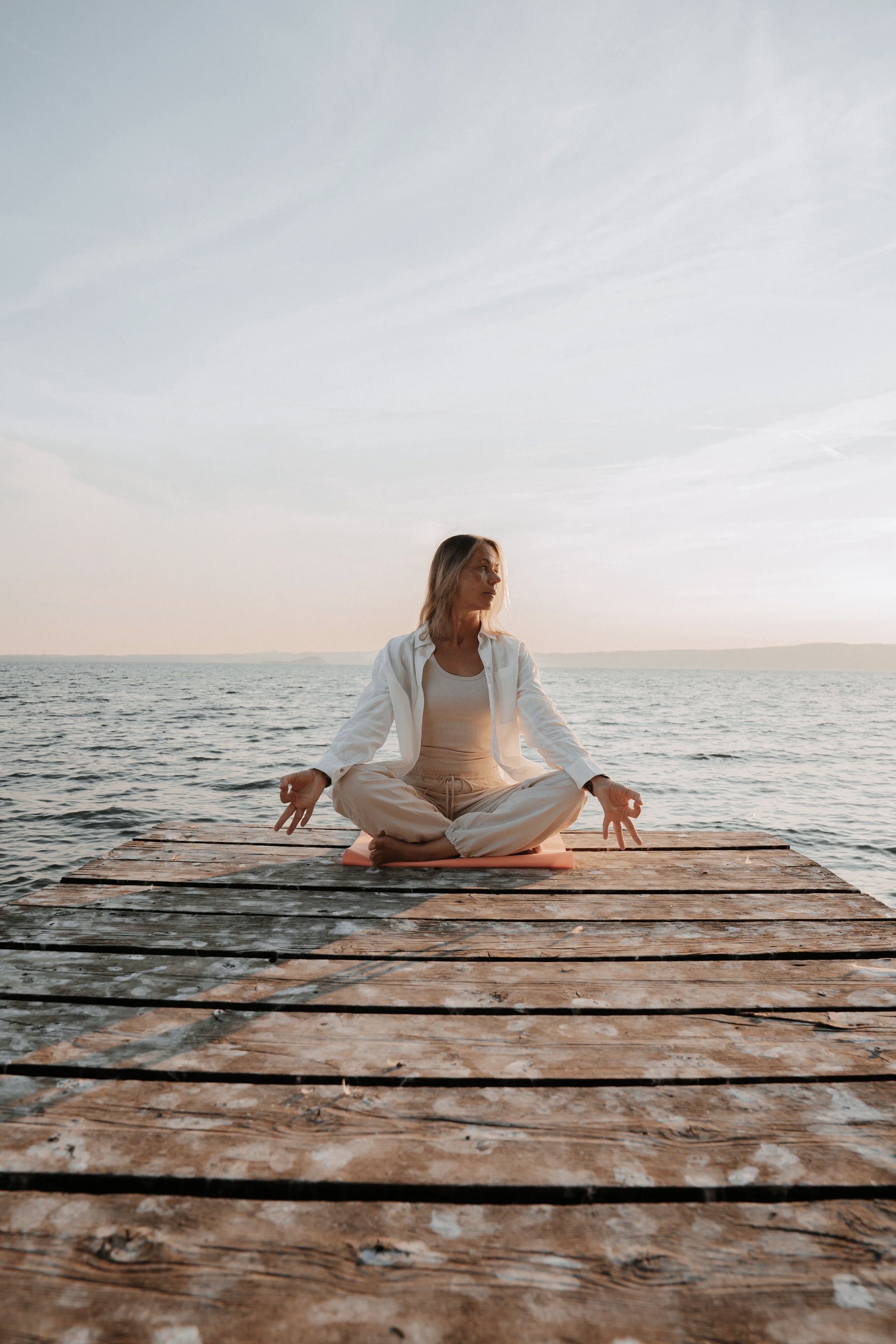Person in Meditationshaltung auf einem Holzsteg am See