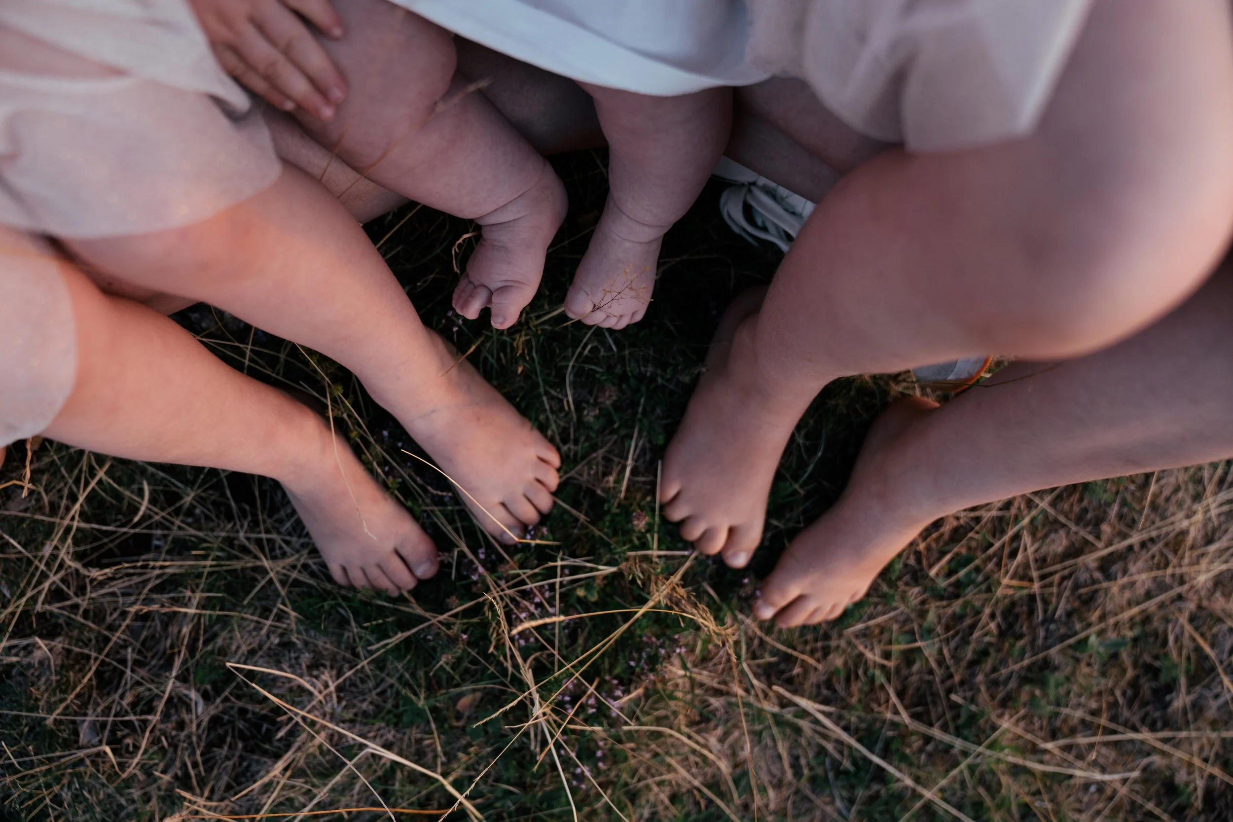 Mehrere nackte Kinder stehen im Kreis auf trockenem Gras und halten sich an den Beinen, wobei sie ihre Köpfe nach innen richten.