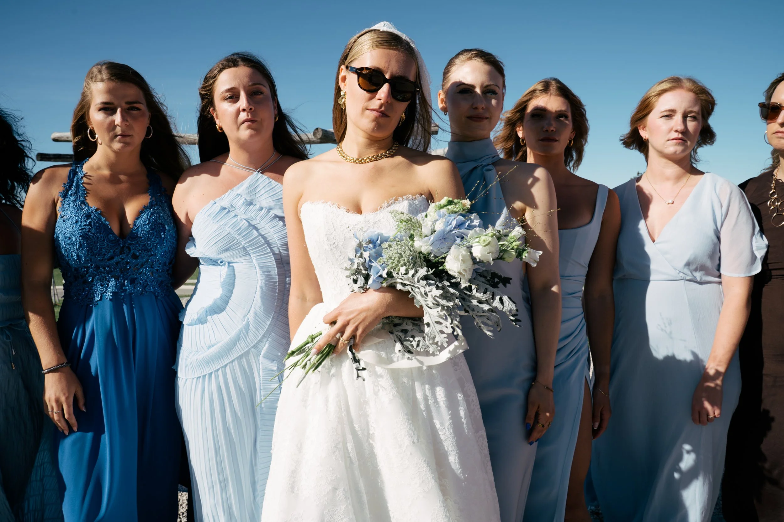 Eine Gruppe von Frauen, vermutlich bei einer Hochzeit, steht draußen an einem sonnigen Tag, mit blauem Himmel im Hintergrund.