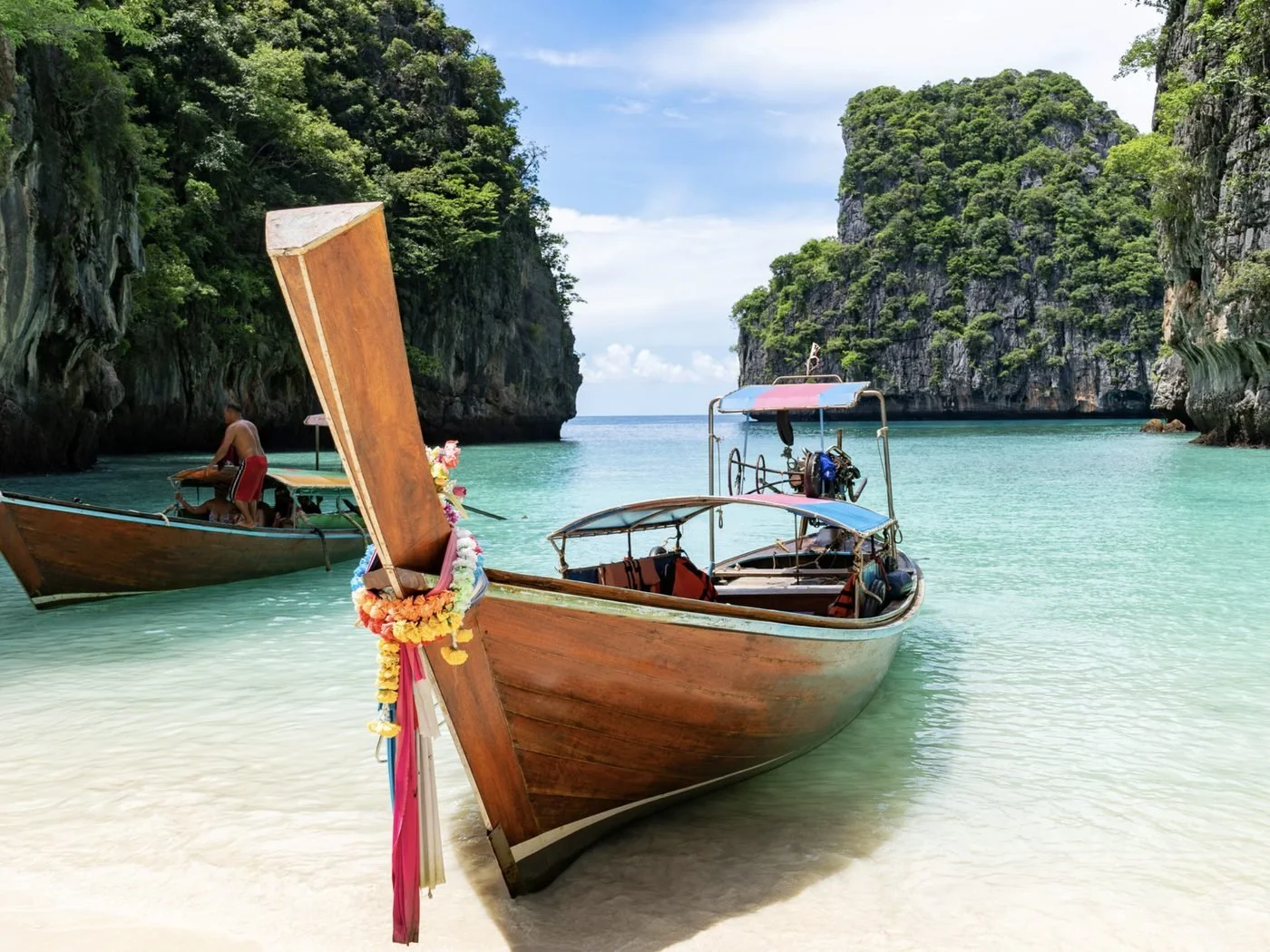 Longtail boats on a white sand beach beneath limestone cliffs in Thailand