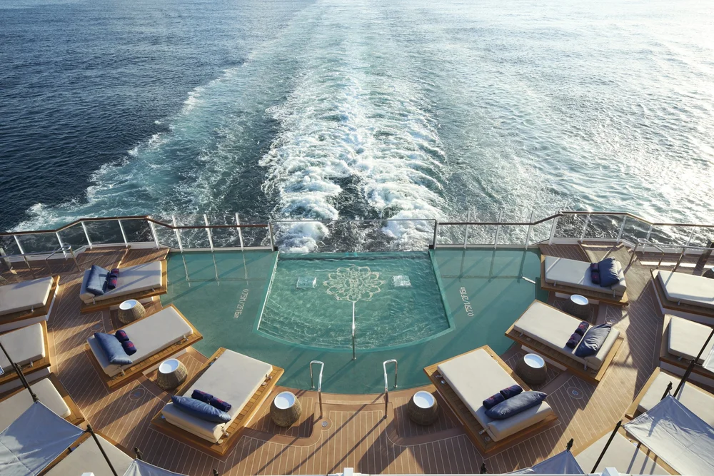 The aft pool and sun loungers on board Explora I, with the ship's wake trailing out to sea