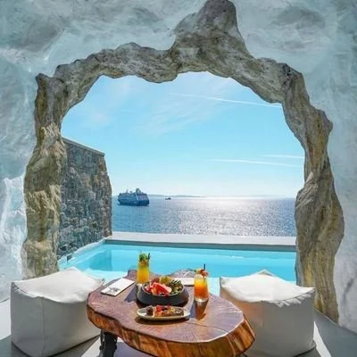 A pool framed by a rock arch looking out to sea and a passing cruise ship
