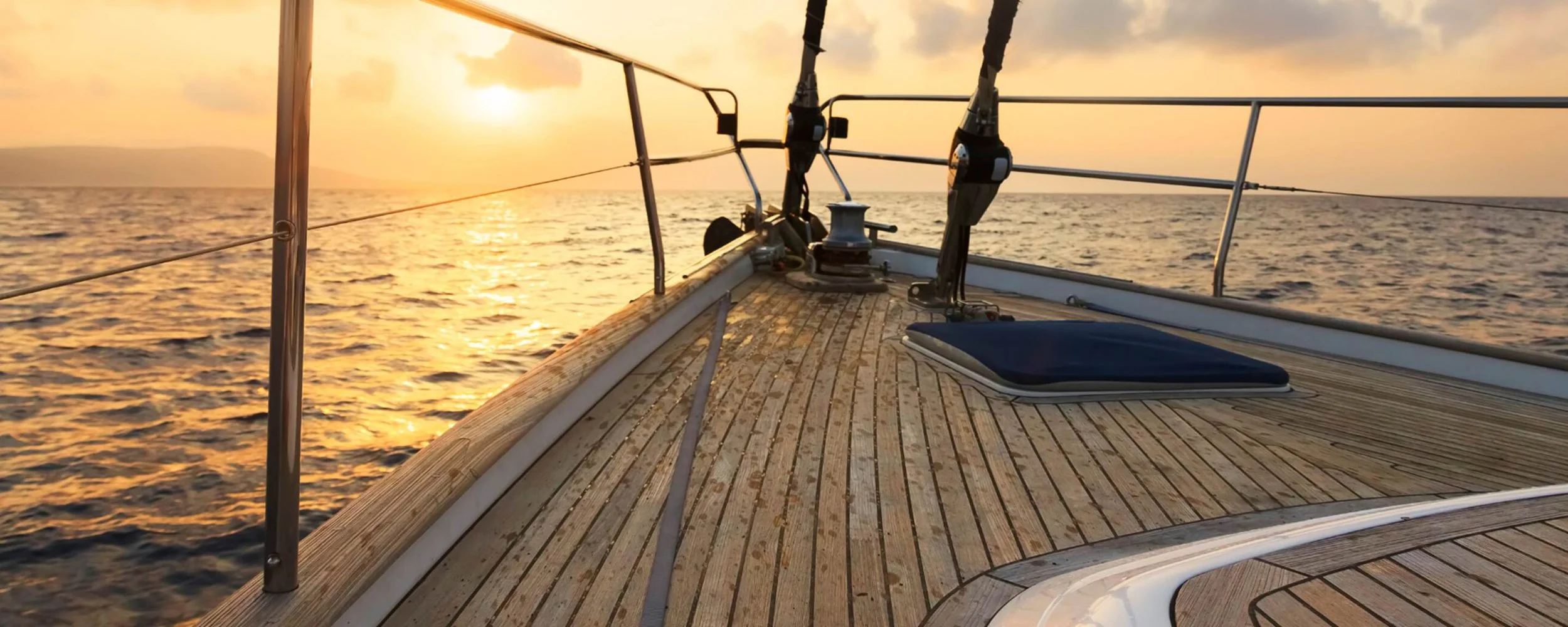 The teak deck and bow of a yacht sailing into a golden sunset