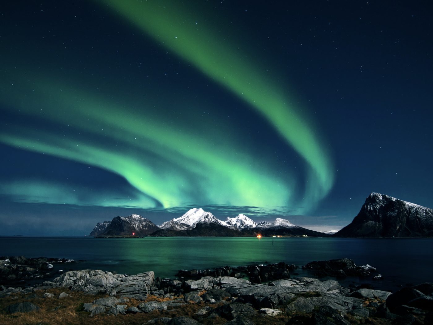 Green Northern Lights over snowy peaks and a fjord in northern Norway
