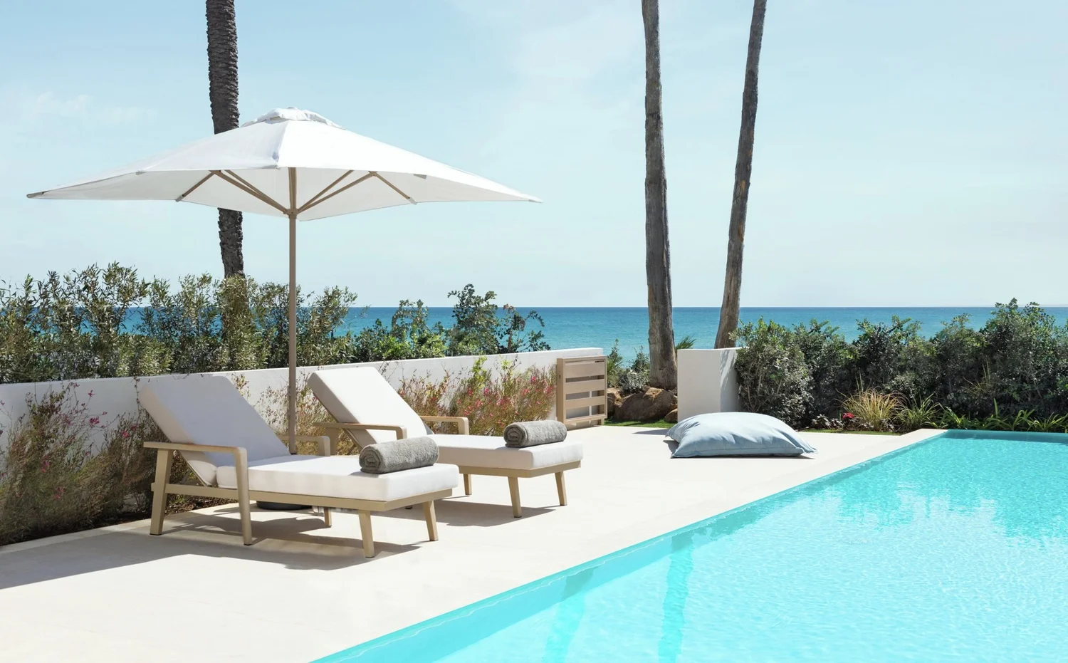Sun loungers, a white parasol and a turquoise pool beside the sea at an Ikos resort