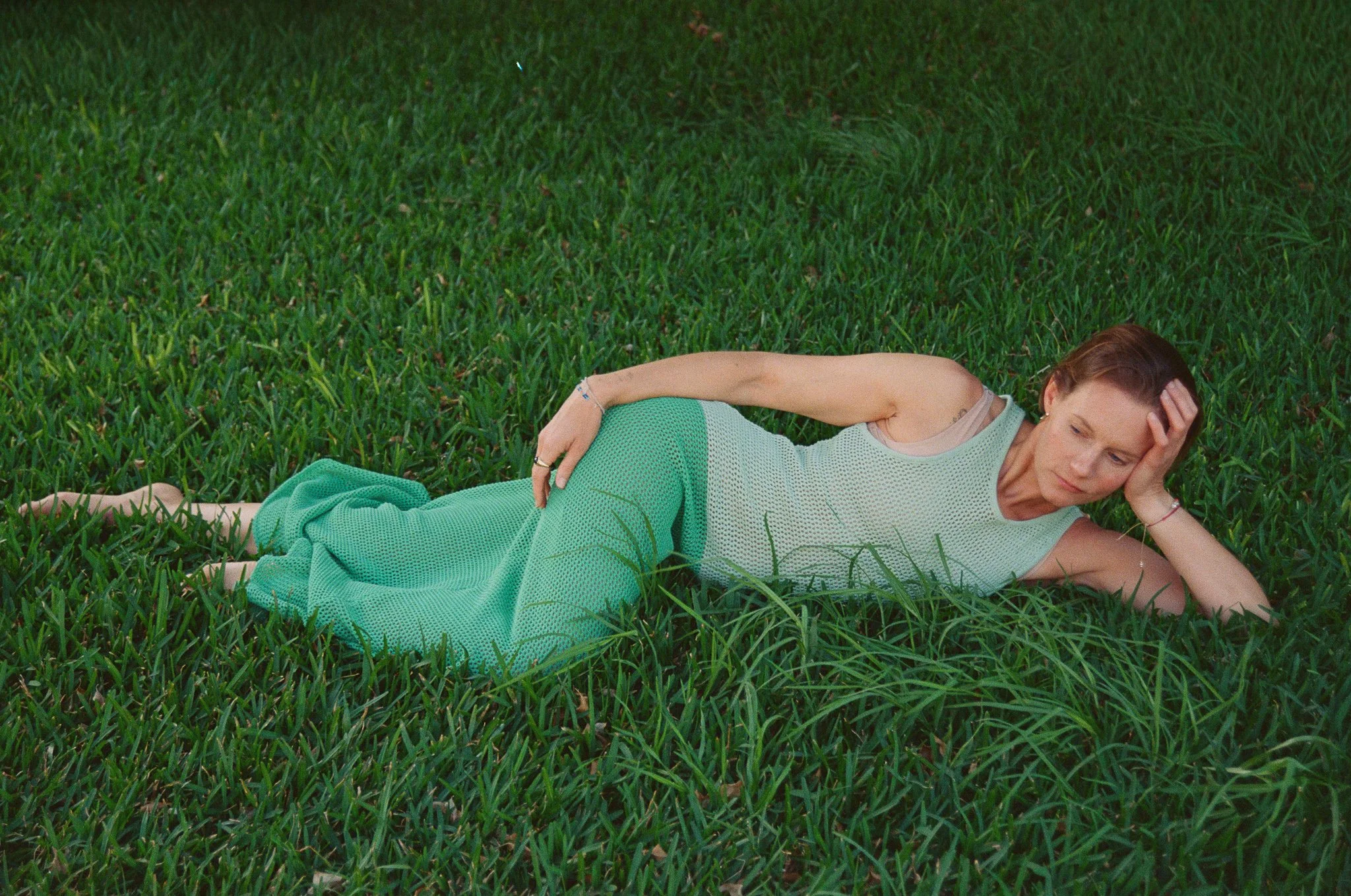 A woman lying on her side on a grassy field, with her head resting on her hand and her eyes closed.
