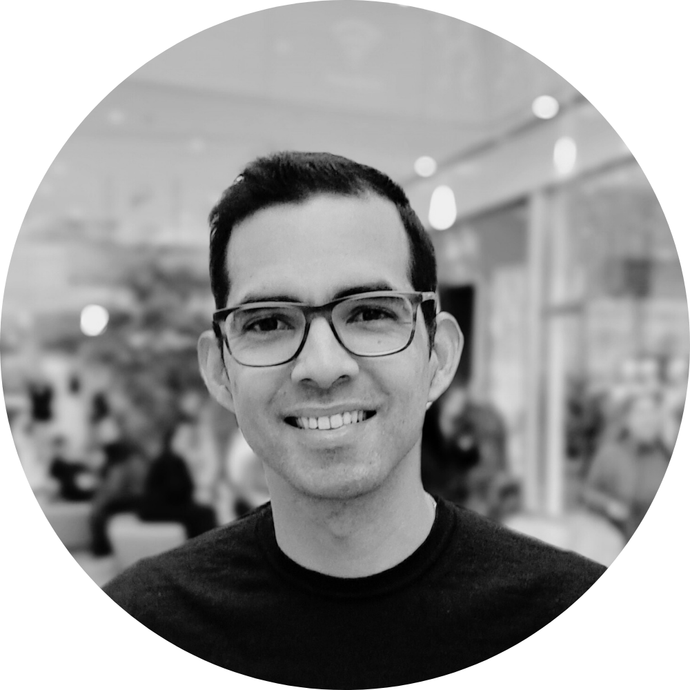 Ritratto di un uomo sorridente con occhiali in un ambiente pubblico, sfocato.