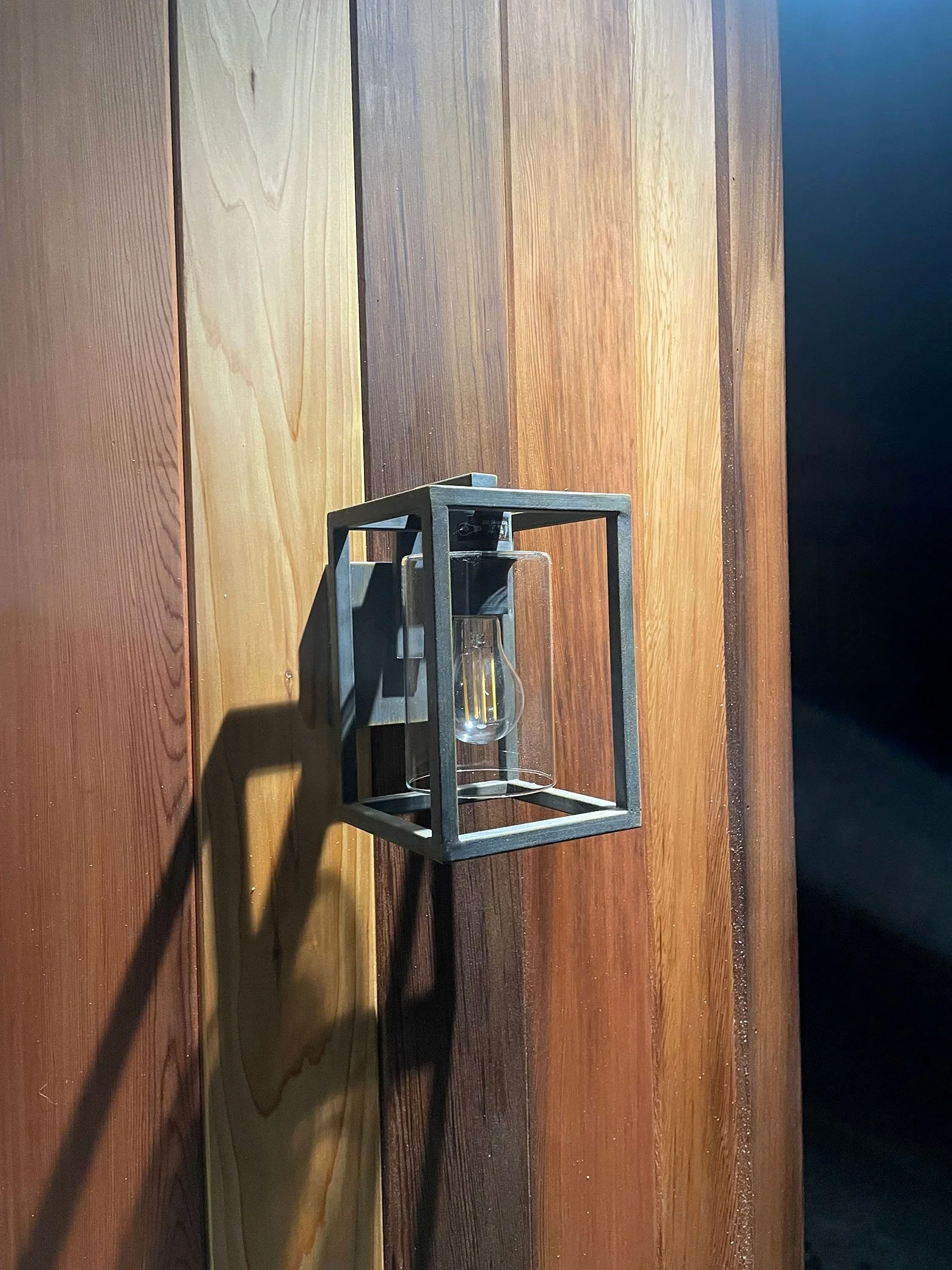  Light fixture casting a glow on a wooden wall outside a garden room. 