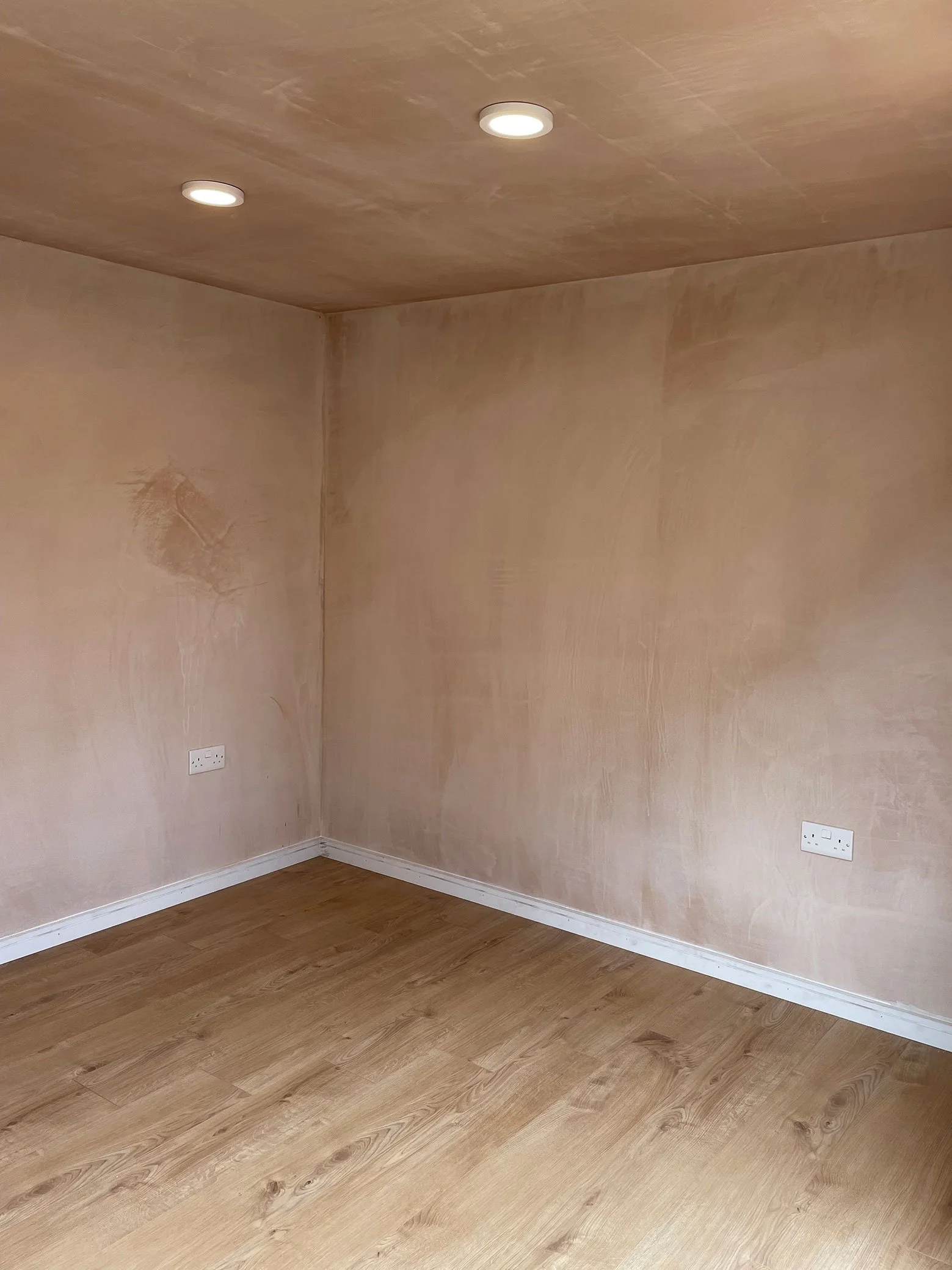  A room with a wooden floor and a wall covered in plaster. 