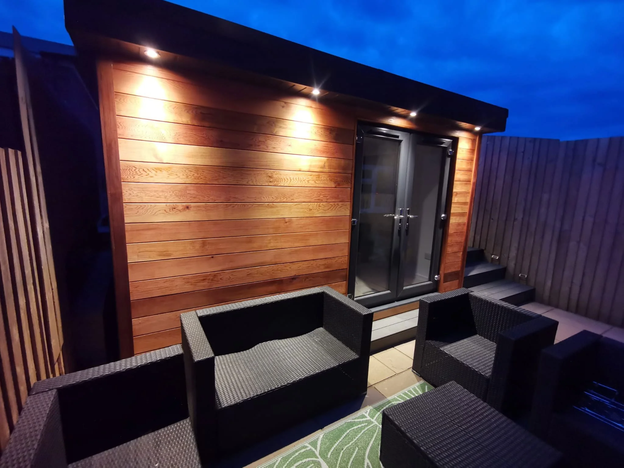  Relaxing wooden deck with modern black furnishings and warm lighting. 