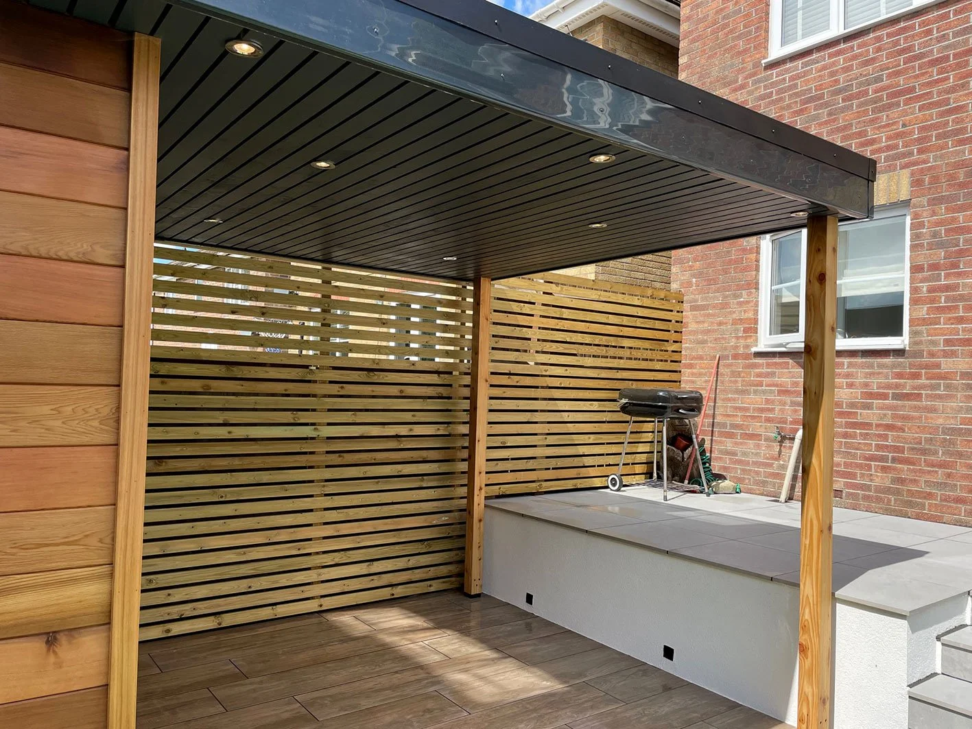  Covered patio featuring a wooden deck and a grill for outdoor cooking. 