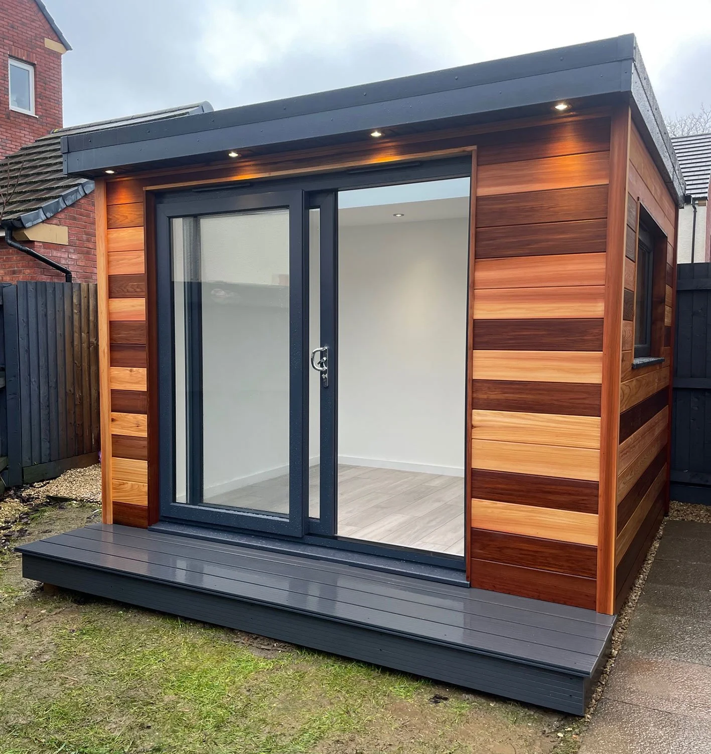  A beautifully designed garden office with sliding doors and a wooden deck, blending seamlessly with the natural surroundings. 