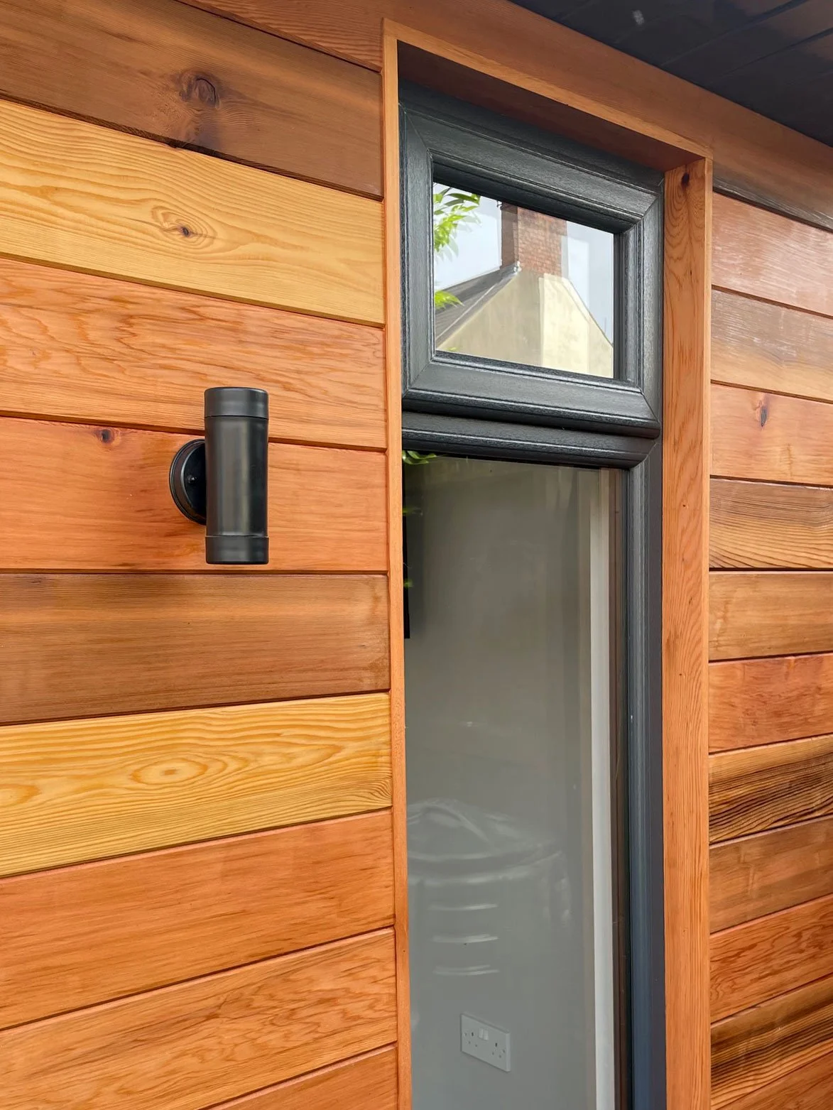  A rustic wooden outdoor room with a window and a door, inviting and full of character. 